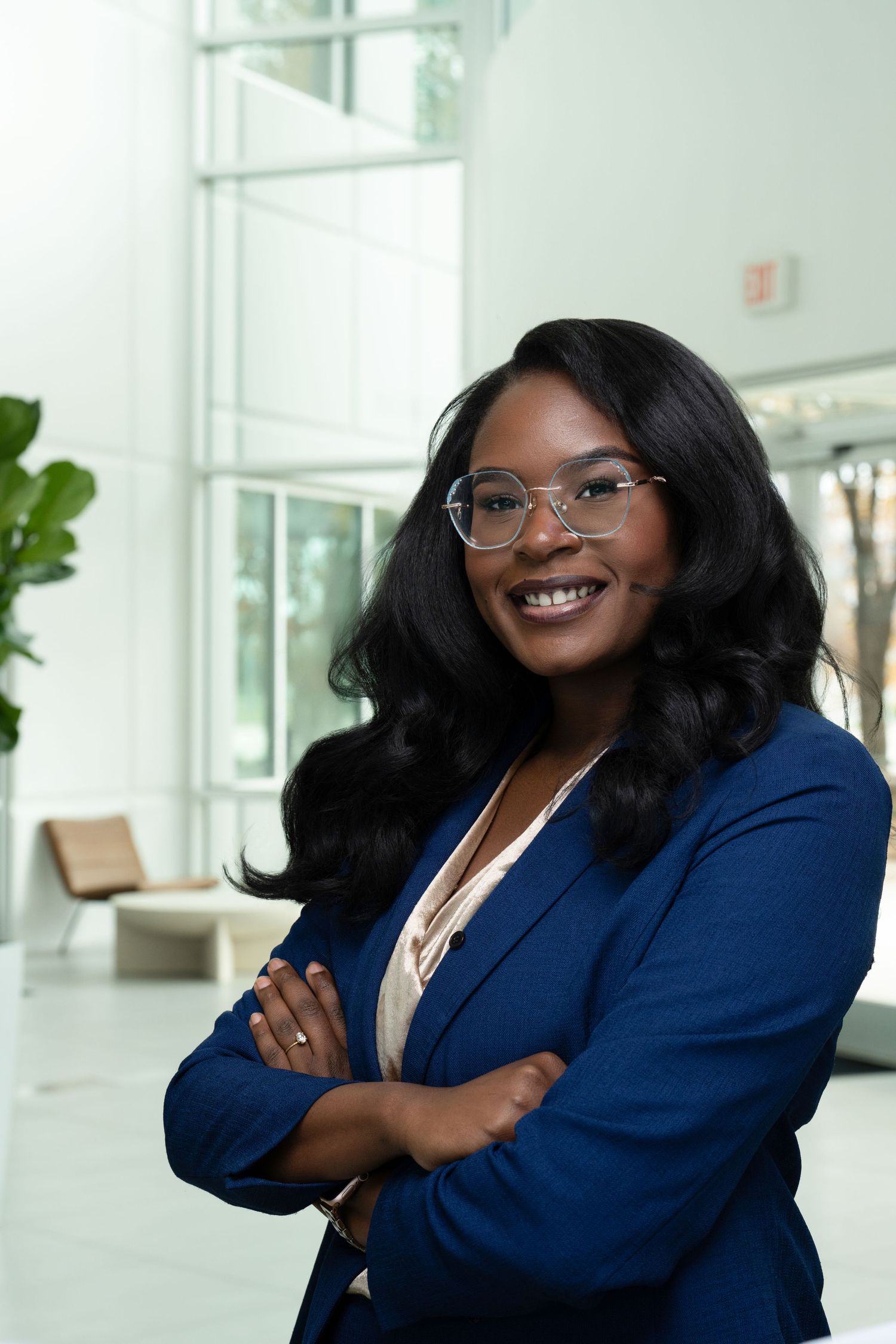 Confident professional in blue blazer and glasses poses with crossed arms in modern office.
