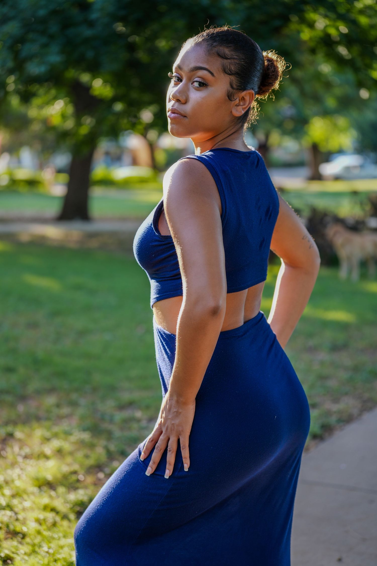 A fashion portrait in a park setting featuring a fitted navy blue two-piece outfit.