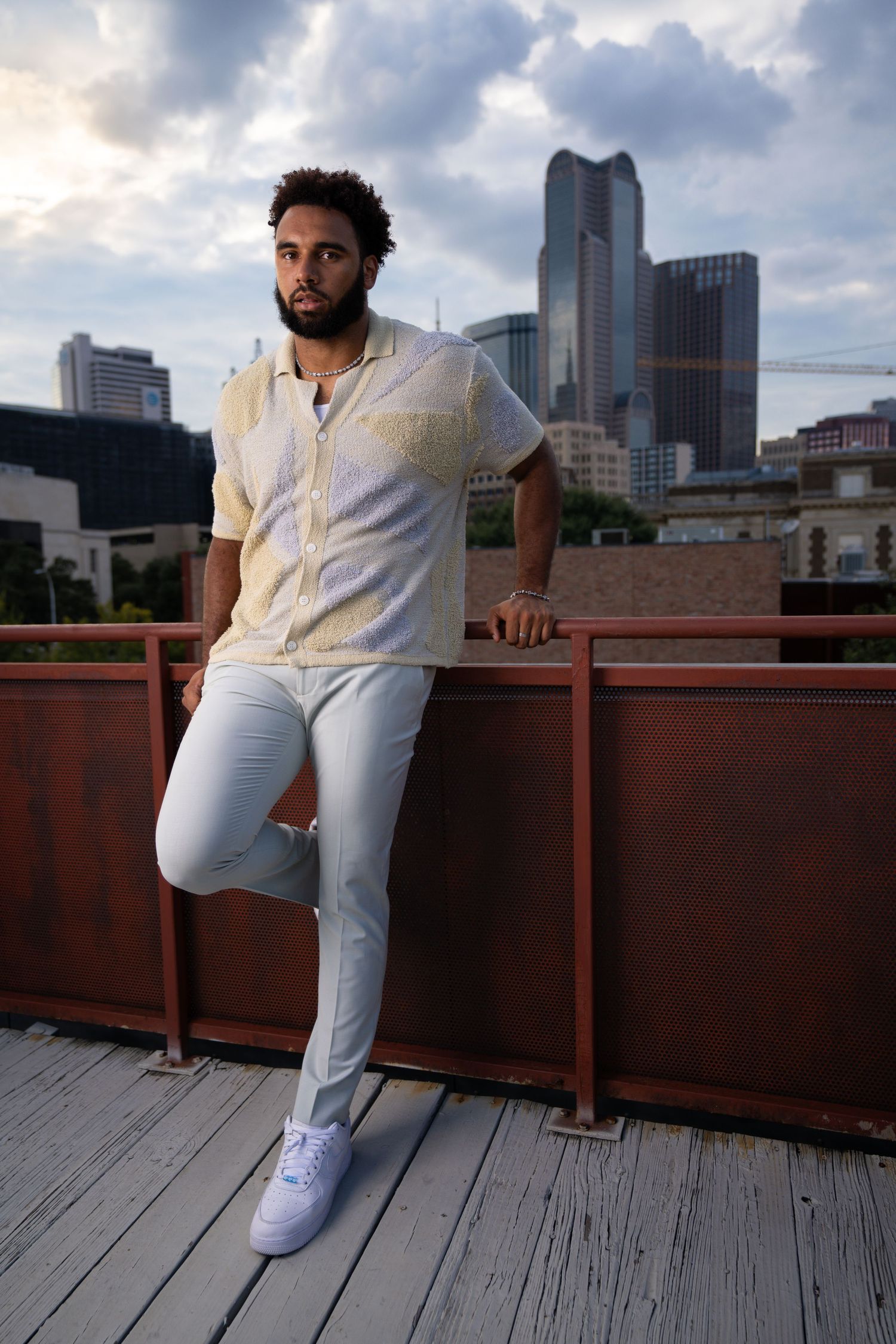 Fashionable rooftop portrait with city skyline backdrop and modern white ensemble.