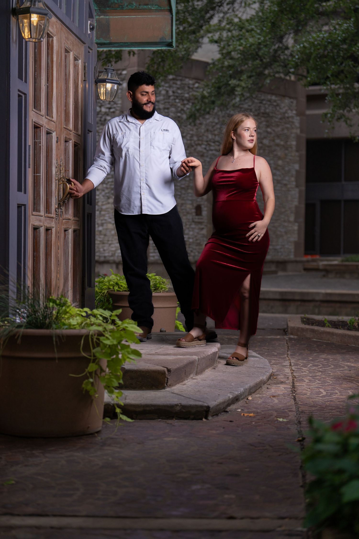 A couple in formal attire performs an elegant dance move on stone steps at dusk, with atmospheric lighting.