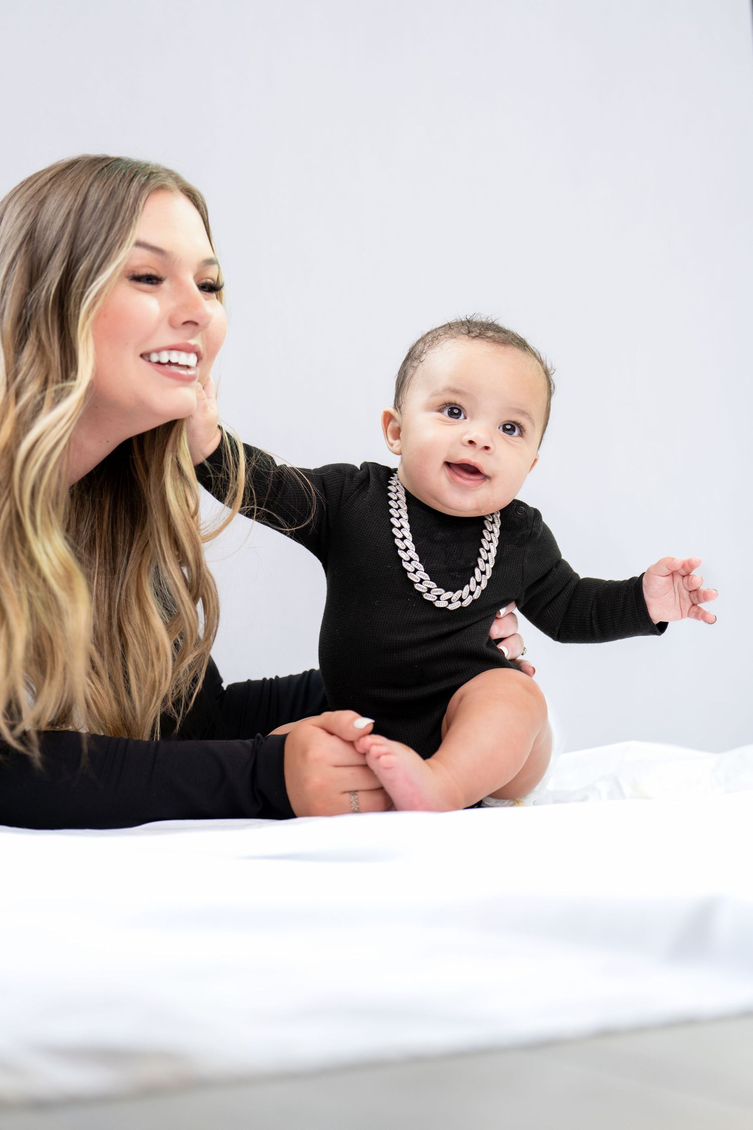 A parent and baby in matching black outfits lie on a white background in a series of tender poses.