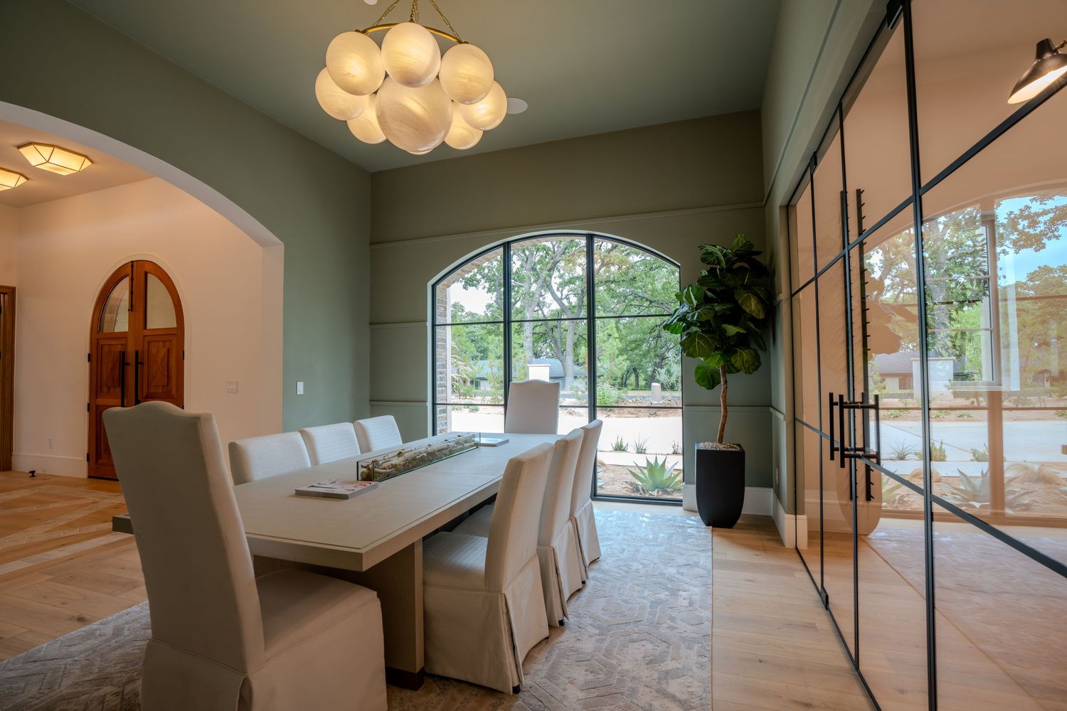 Modern dining space with glass walls, statement chandelier and neutral color scheme.