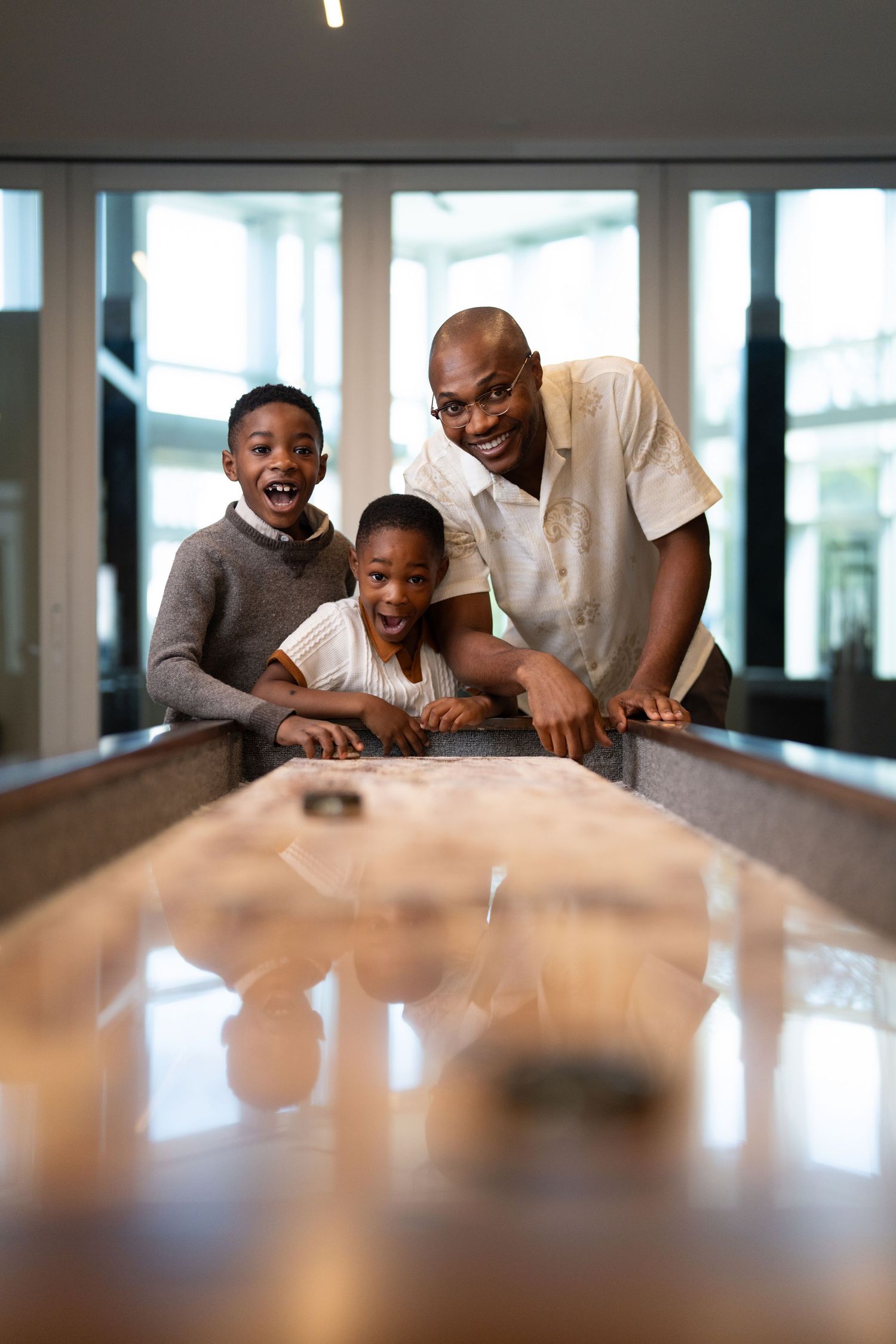 Three people enjoying a game of shuffleboard together in a bright indoor space.