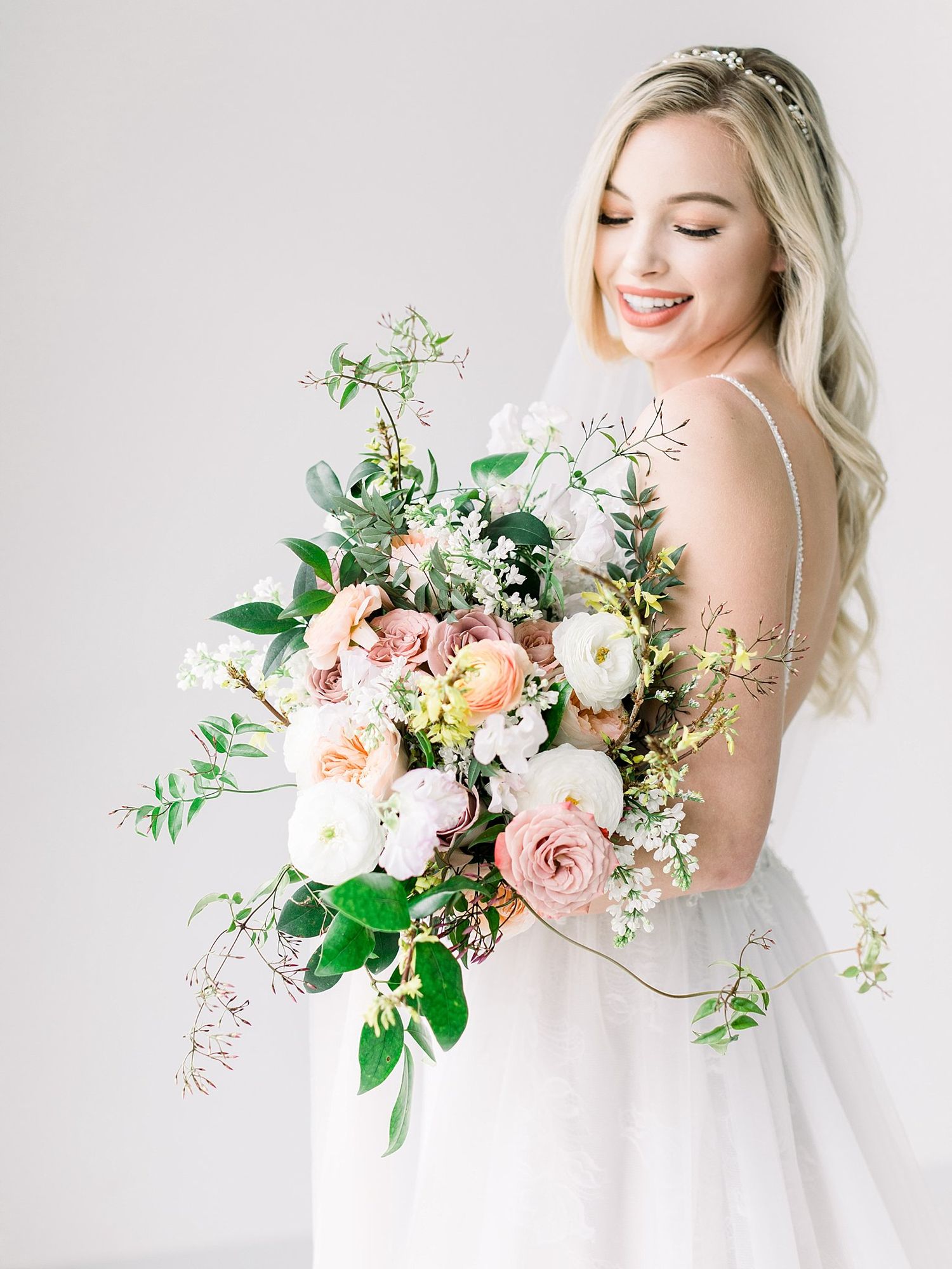 Ethereal bridal portraits showcase elegant white dress and romantic peach and cream floral bouquet against light backdrop.