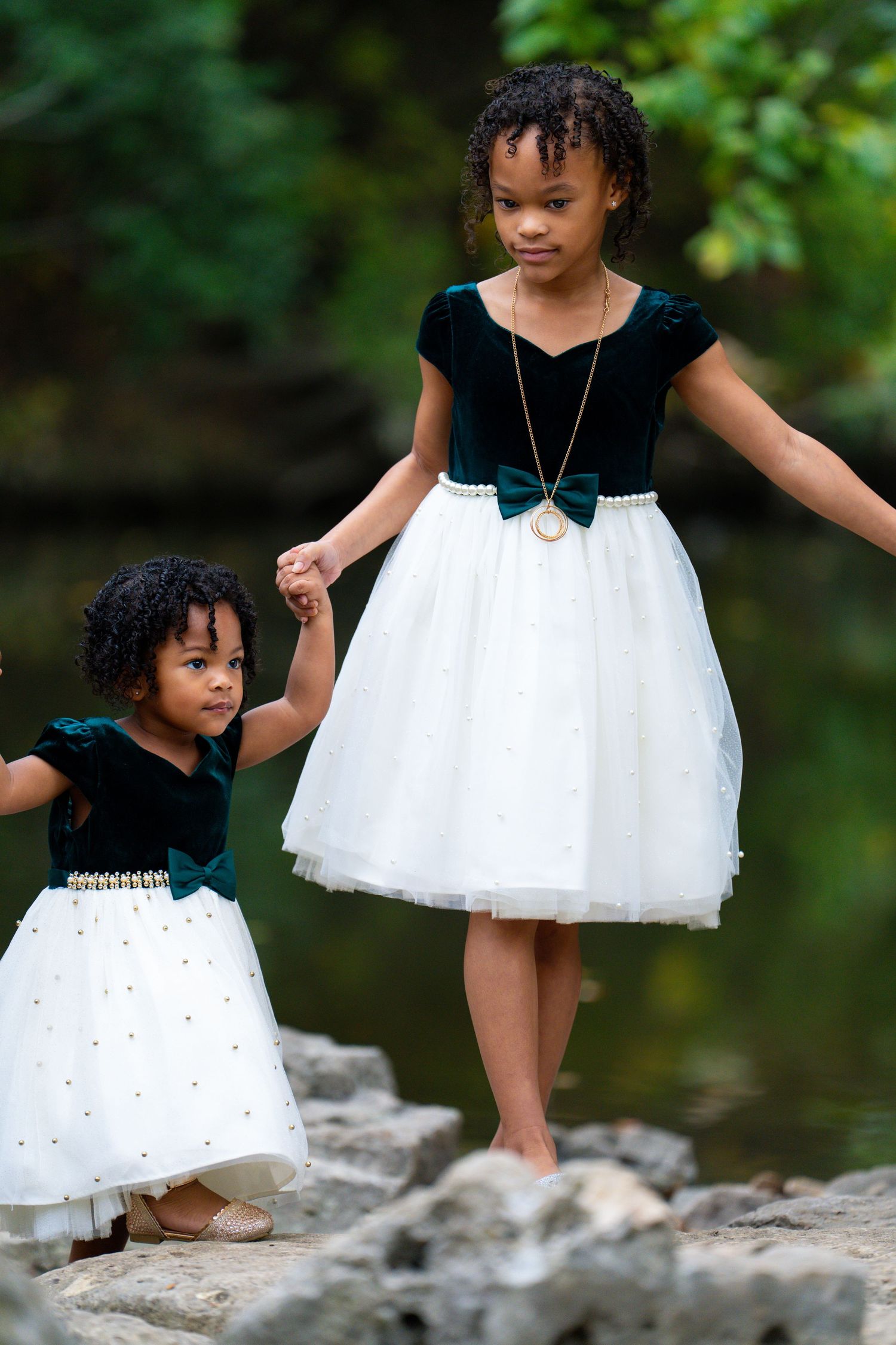 Two children in matching black and white dresses holding hands while standing on rocks.