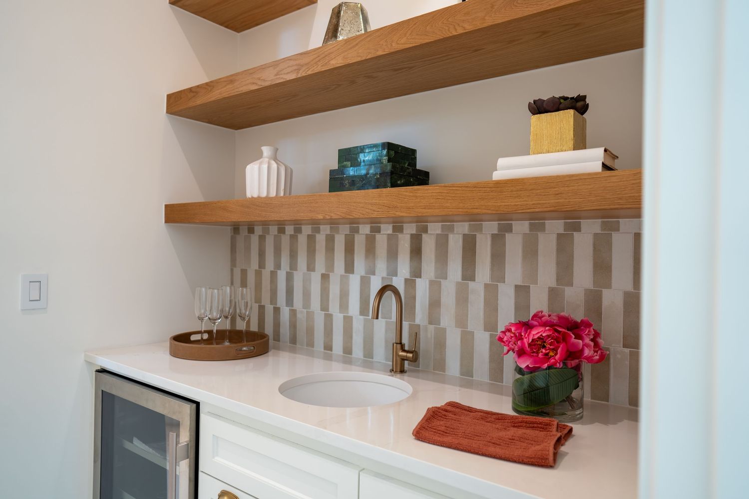 Built-in bar area with wooden shelving, textured backsplash and mini fridge.