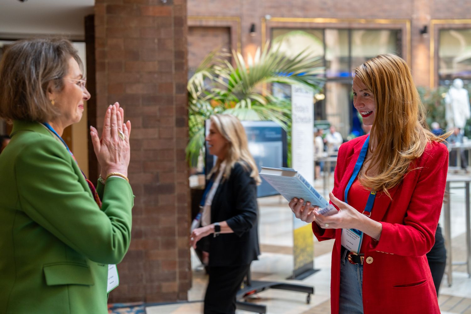 Two professionals engaged in conversation outside a brick building, with one wearing a red blazer and another in green.