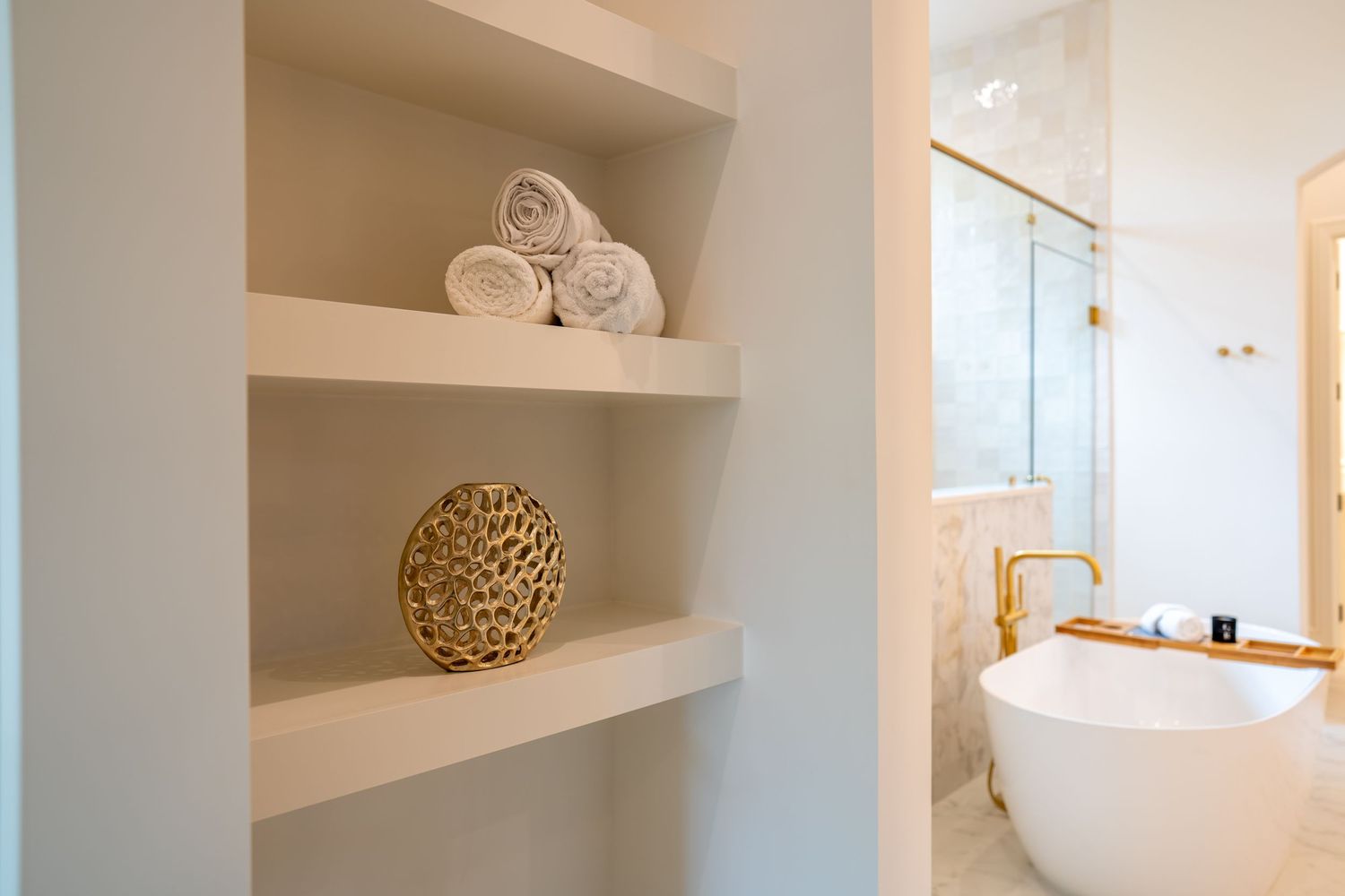 Built-in bathroom shelving with decorative accessories and glimpse of freestanding tub.