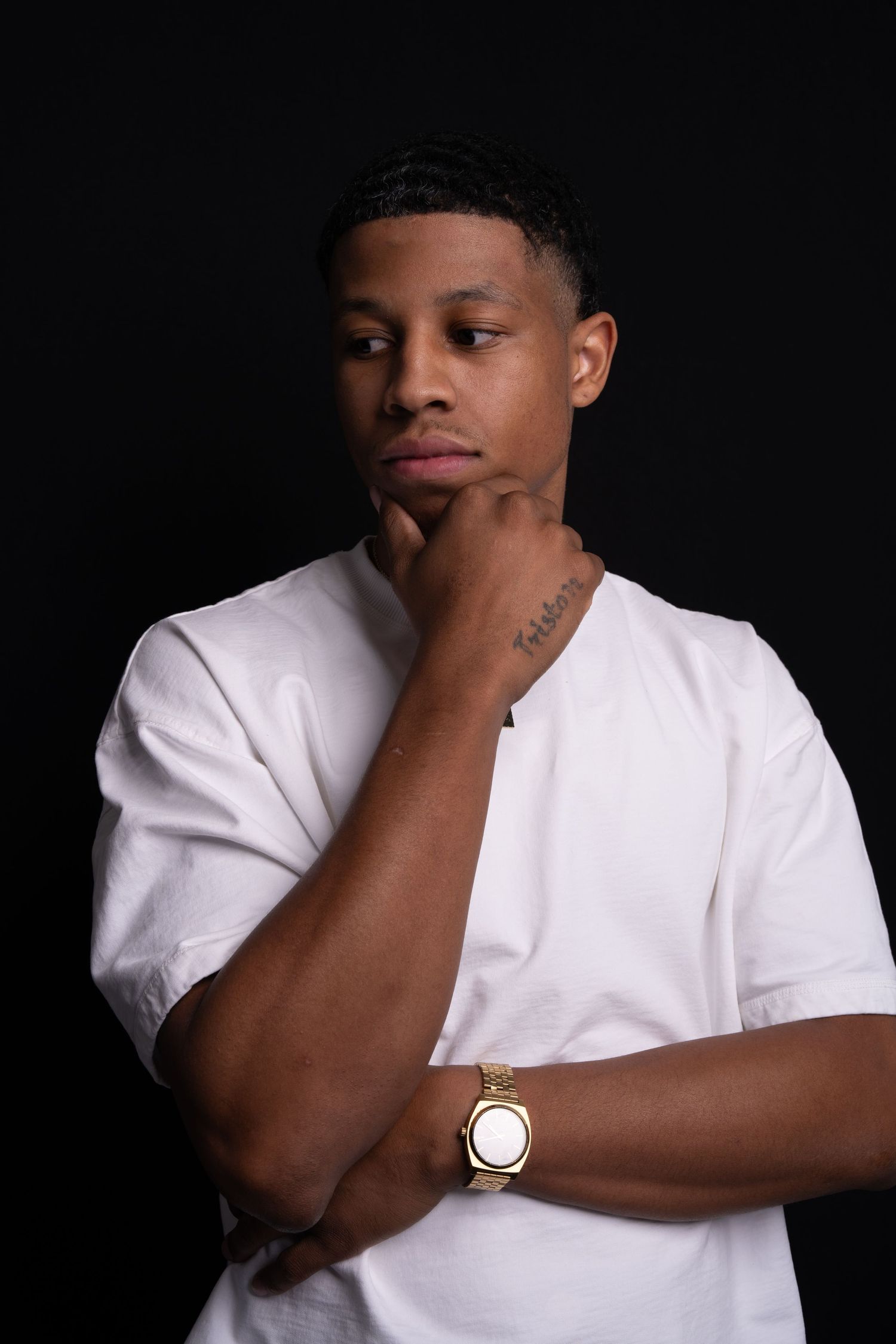 Thoughtful studio portrait of a person in white t-shirt against dark background with watch.