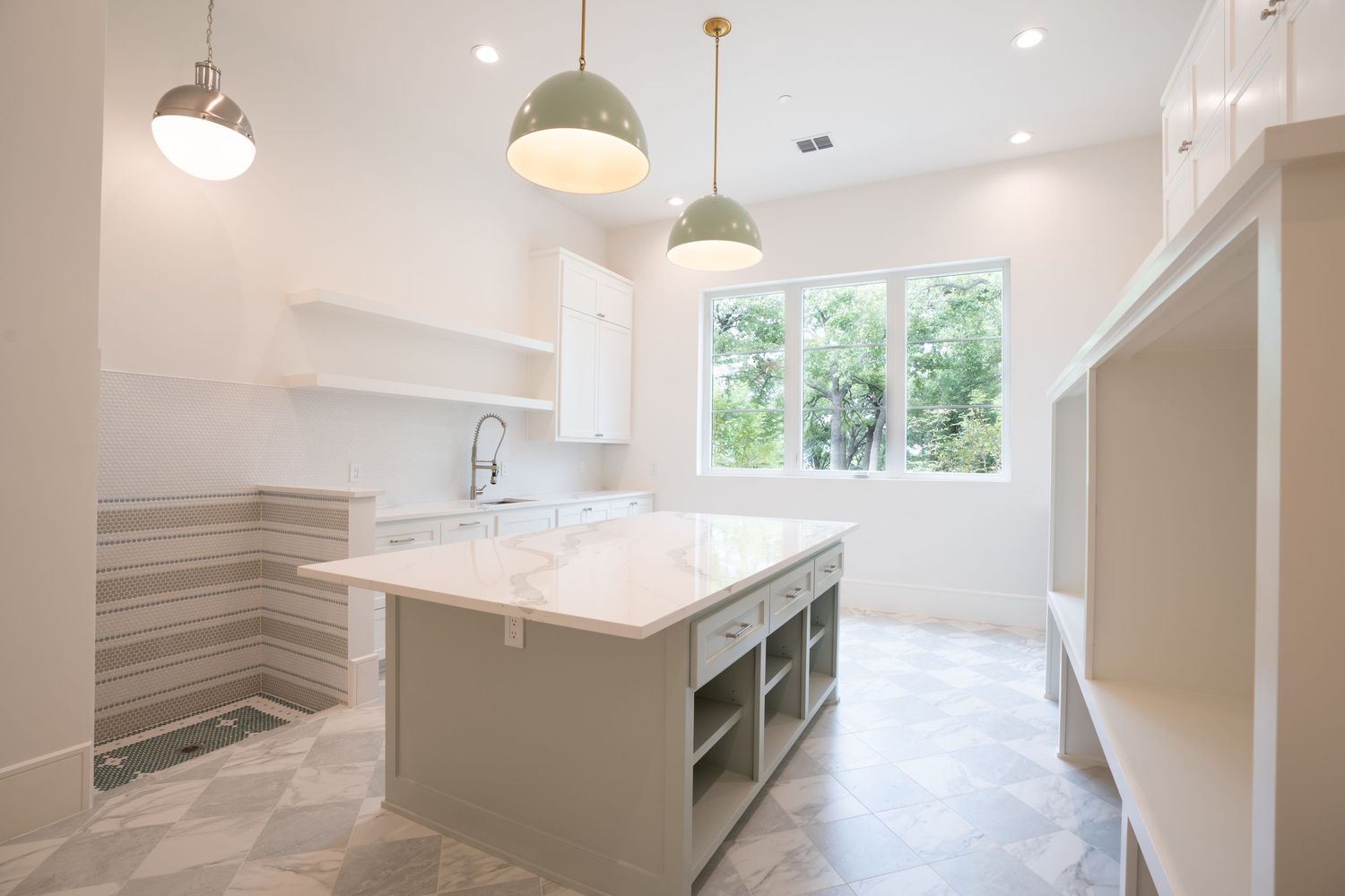 Bright white kitchen with marble countertops, floating shelves and large windows overlooking greenery.