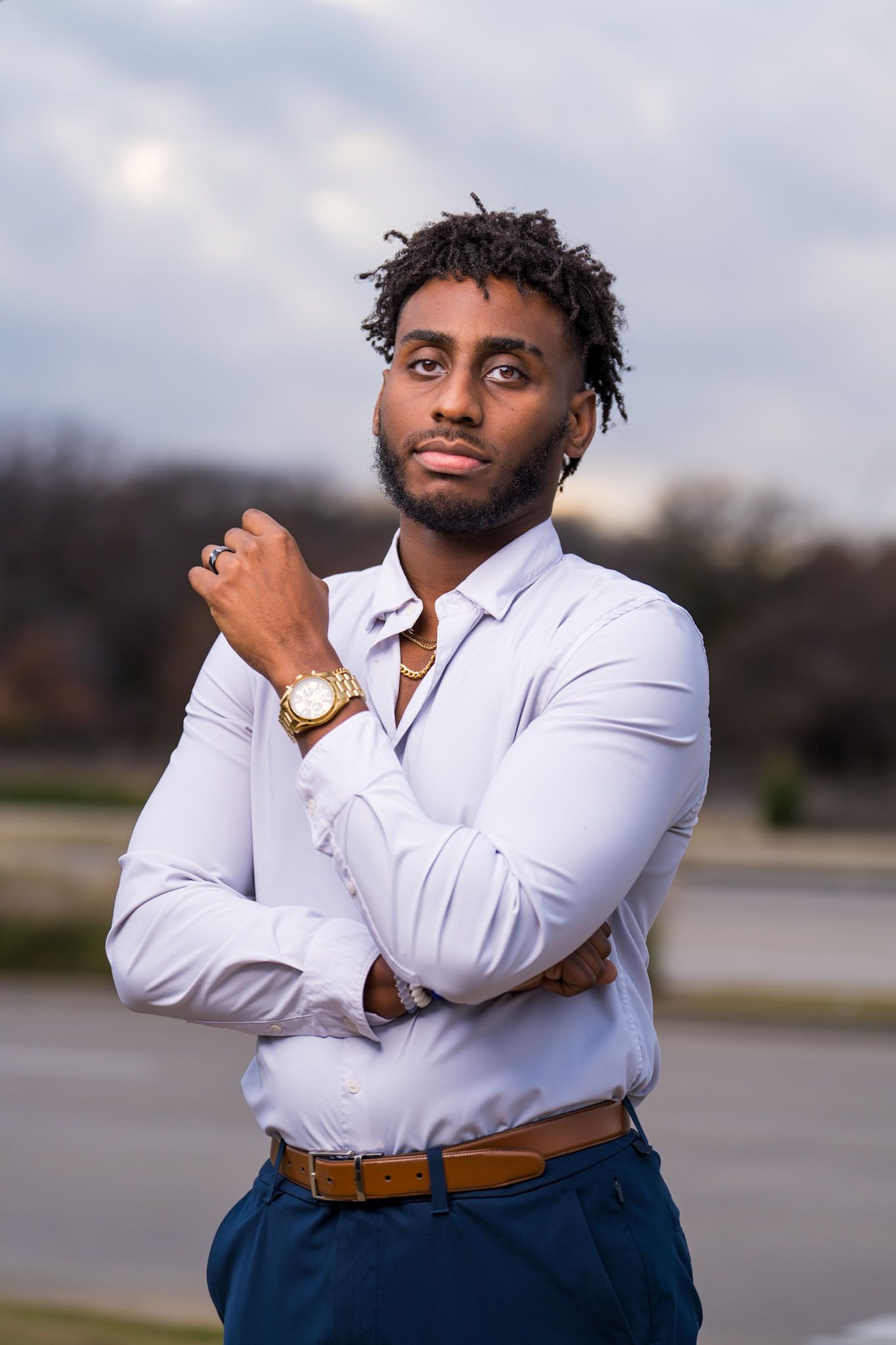 Business attire with white fitted shirt and brown belt against cloudy backdrop.