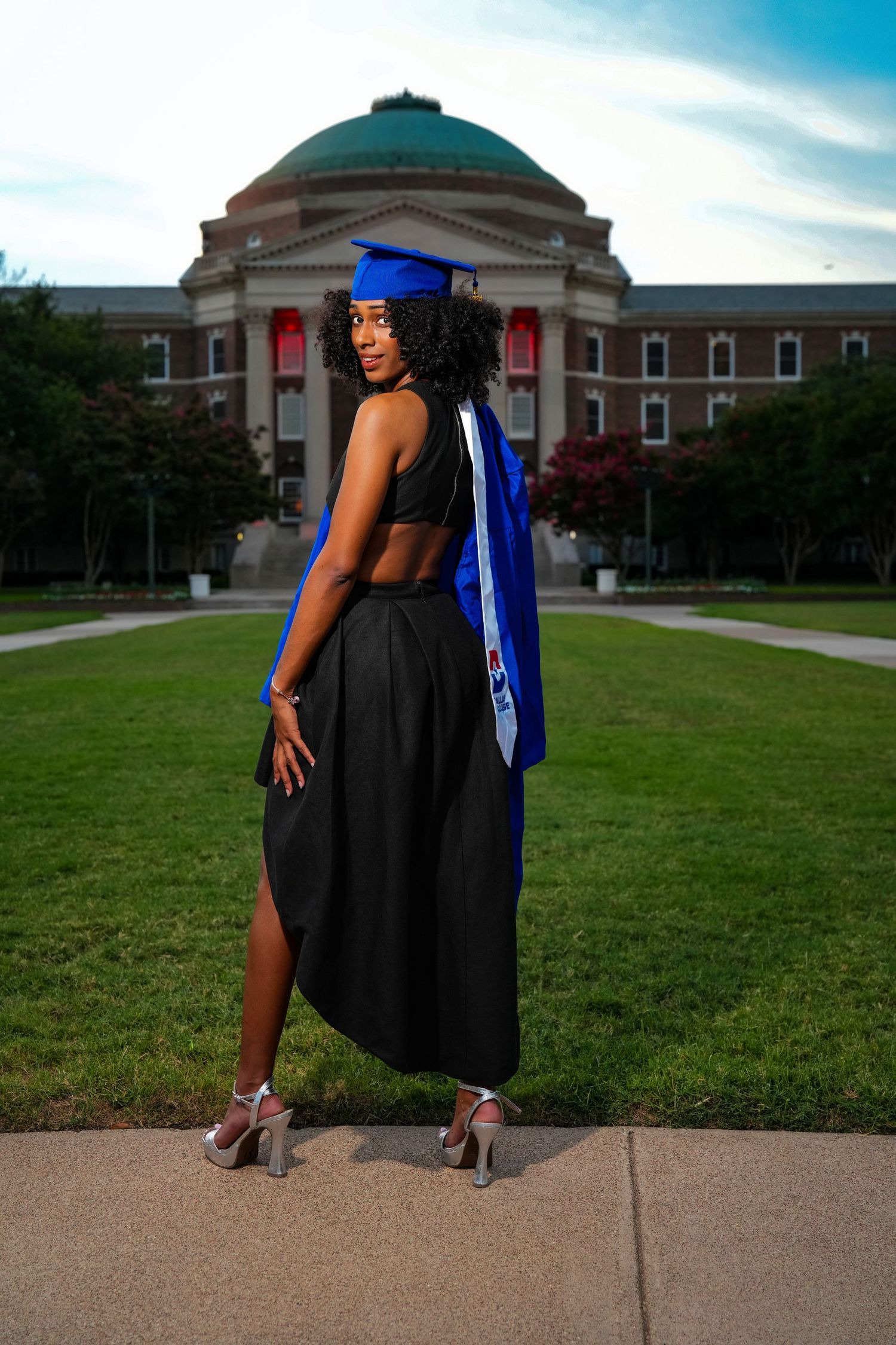 Graduate poses in front of historic university building during sunset celebration.