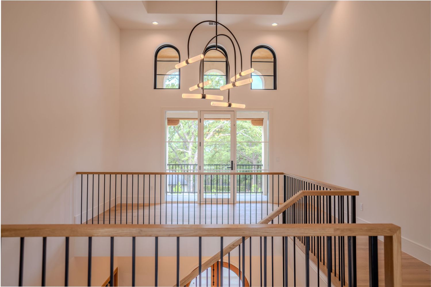 Contemporary staircase landing with black metal railings and arched window chandelier.