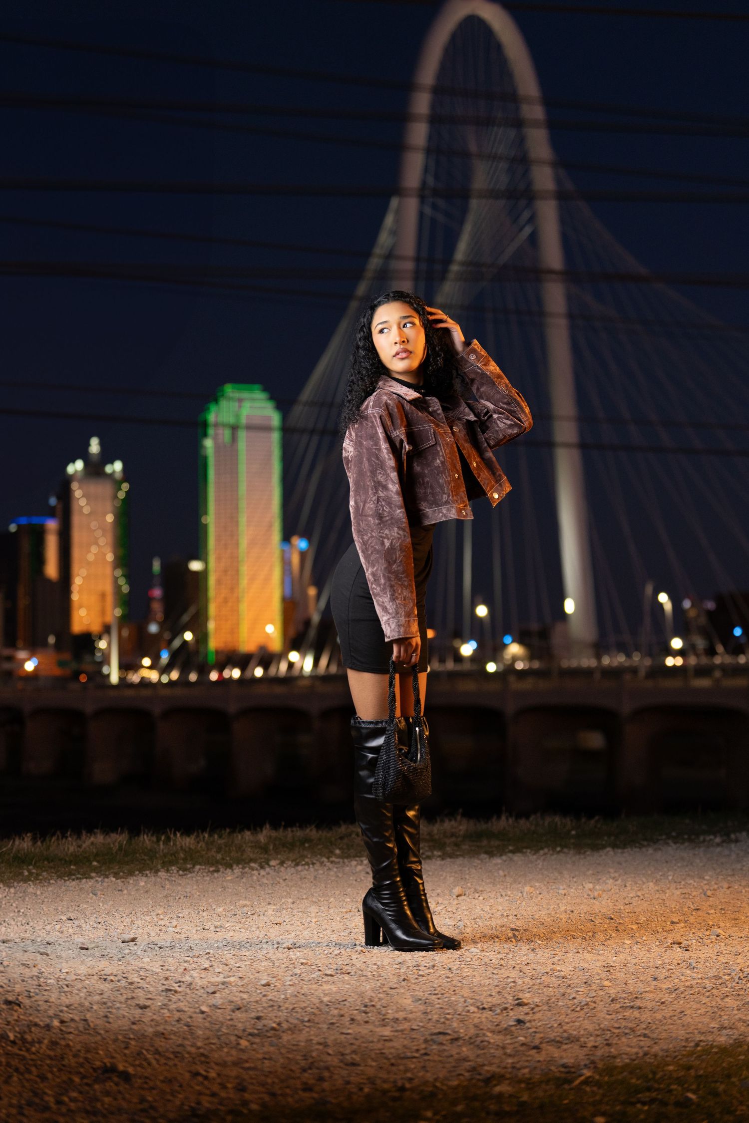 Fashion portrait at night with illuminated Margaret Hunt Hill Bridge and Dallas skyline in background.