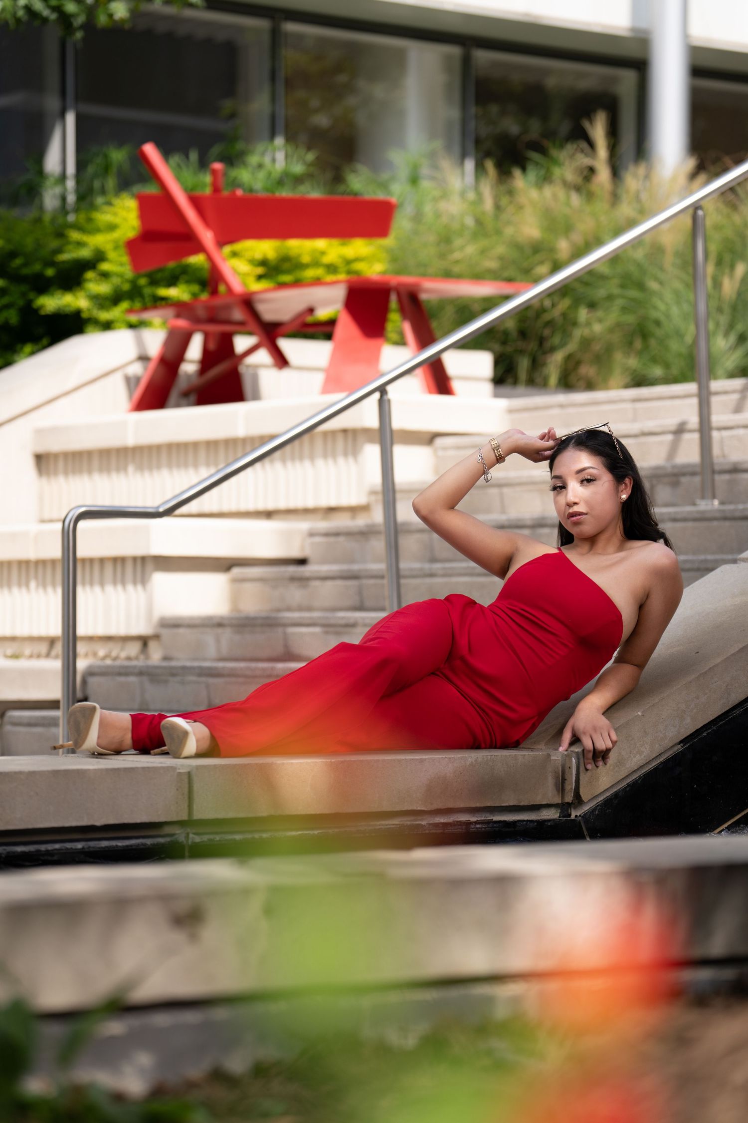 Someone in a flowing red dress reclines gracefully on outdoor steps in an artistic photoshoot sequence.