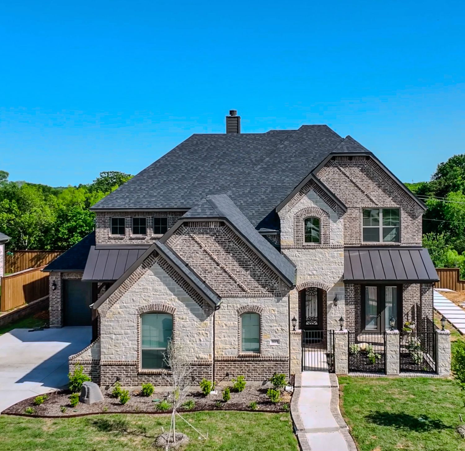 Luxury stone and brick house with metal roof accents and manicured landscaping.