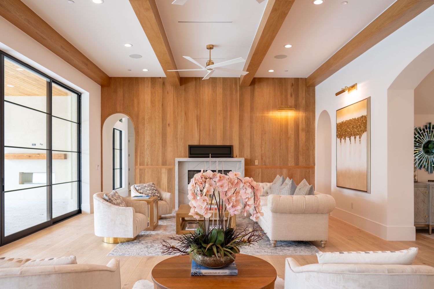 Contemporary living room with wood beam ceiling, large windows, and comfortable white seating.