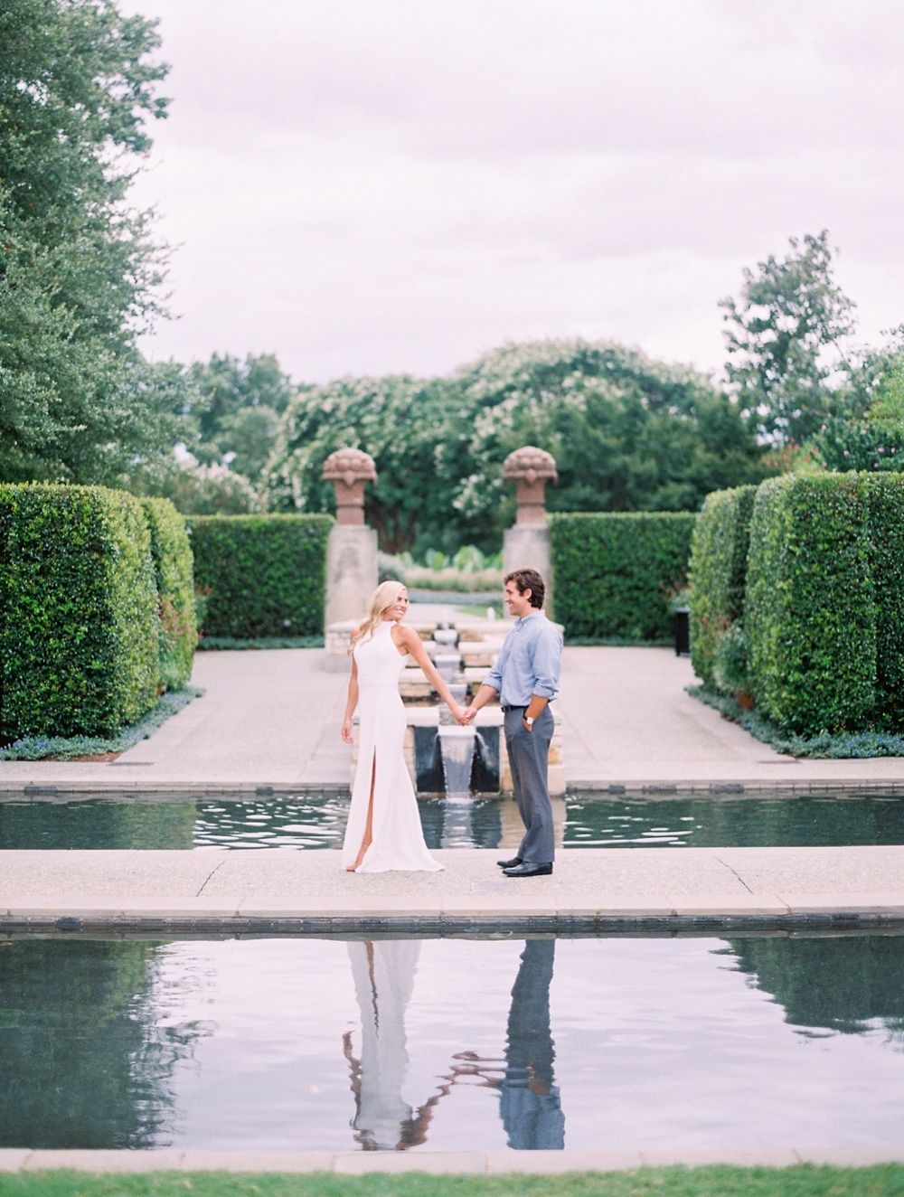 Elegant wedding photo shoot at a formal garden setting with reflection pool and manicured hedges.
