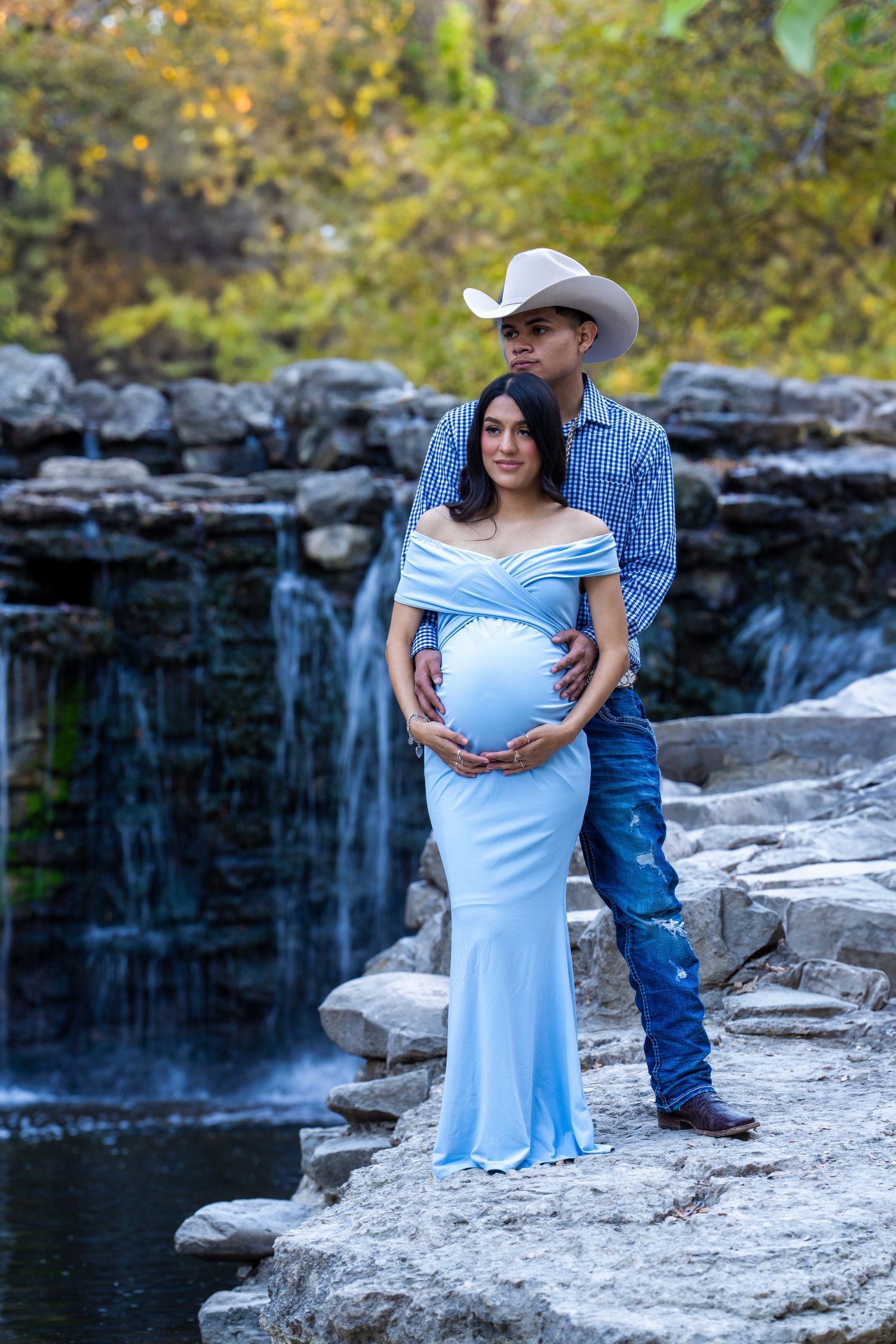 A maternity photo featuring couple by waterfall with person wearing flowing blue dress.
