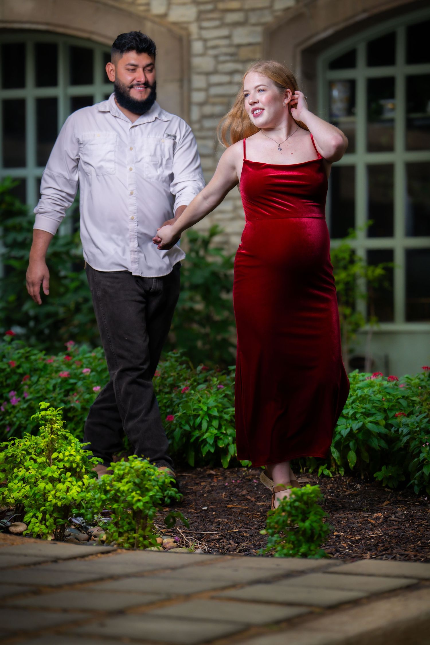 Couple enjoying moment together in garden setting, woman wearing red velvet dress.