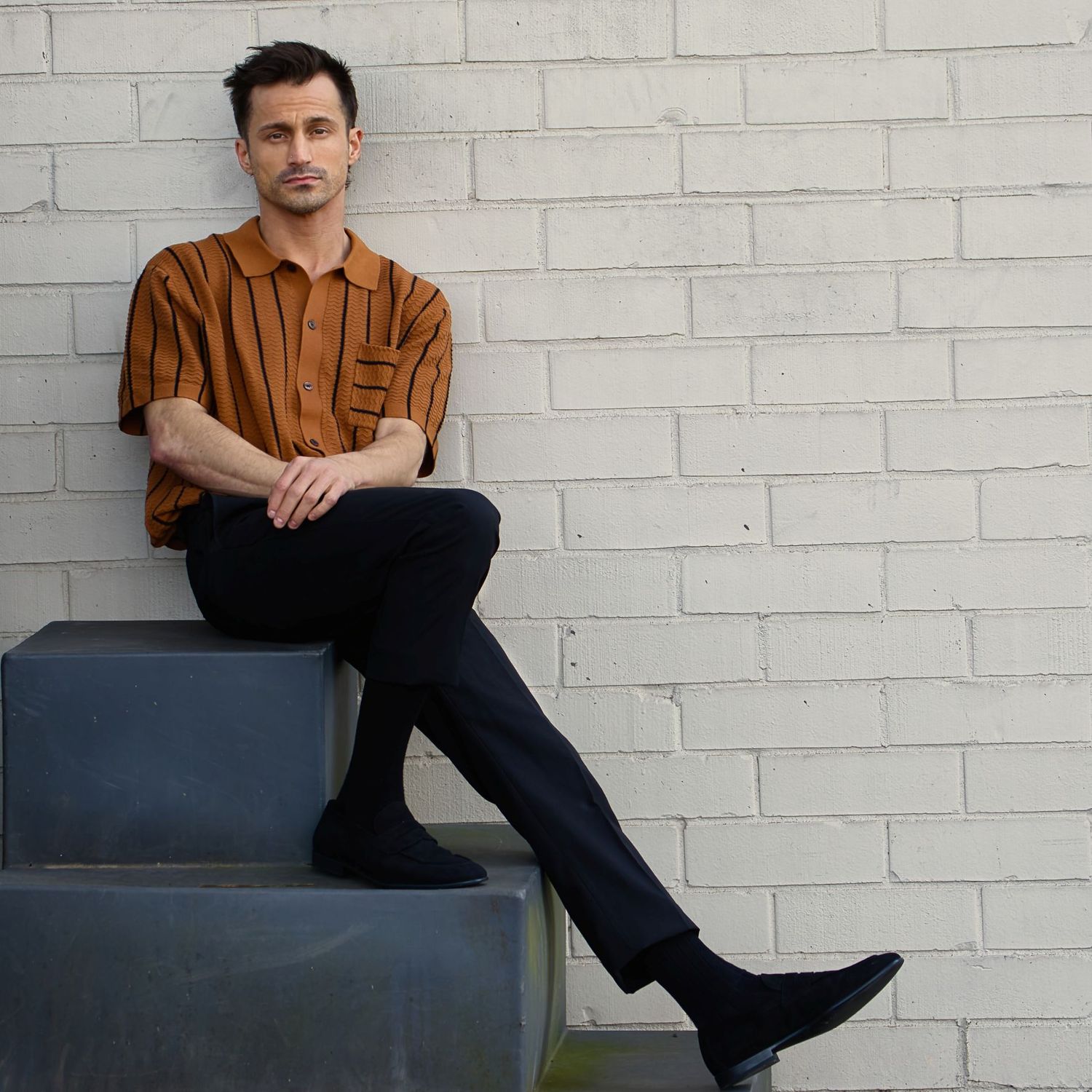 Casual lifestyle portraits against white brick wall wearing brown button-up shirt.