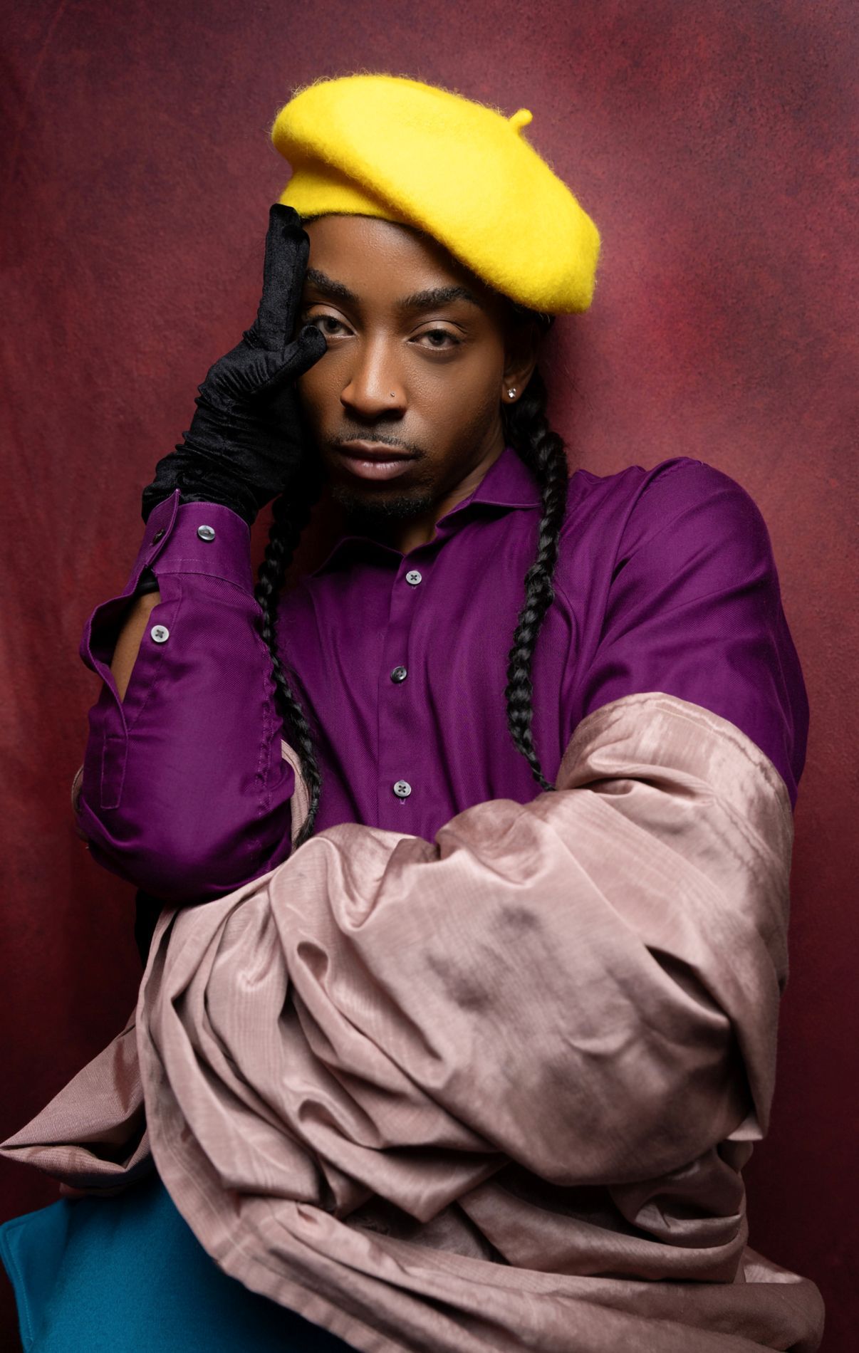 A person in a purple jacket and yellow beanie poses against a dark red background in a stylish fashion portrait series.