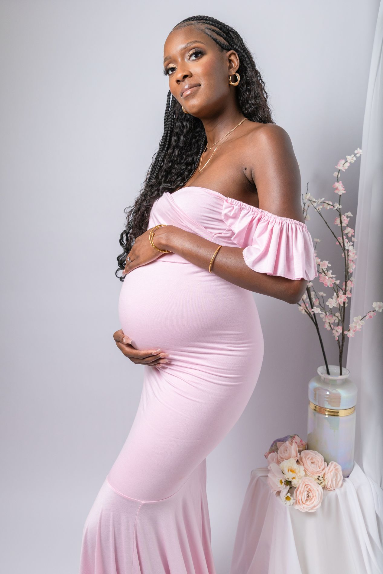 Maternity portrait of an expectant mother in a pink off-shoulder gown against a light background.