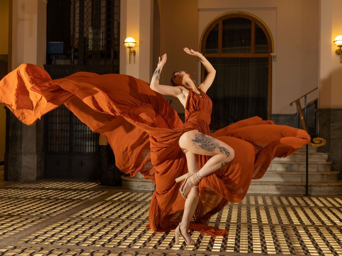 Dancing figure in flowing orange dress creates motion against classic interior architecture.