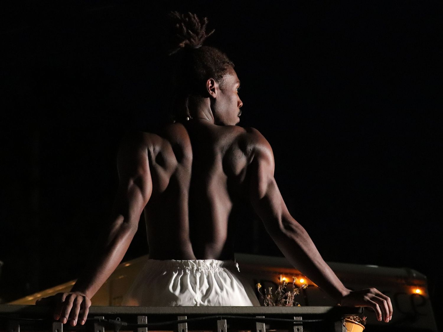 Dramatic silhouette of a muscular performer leaning back against a piano in dark lighting with dramatic shadows.