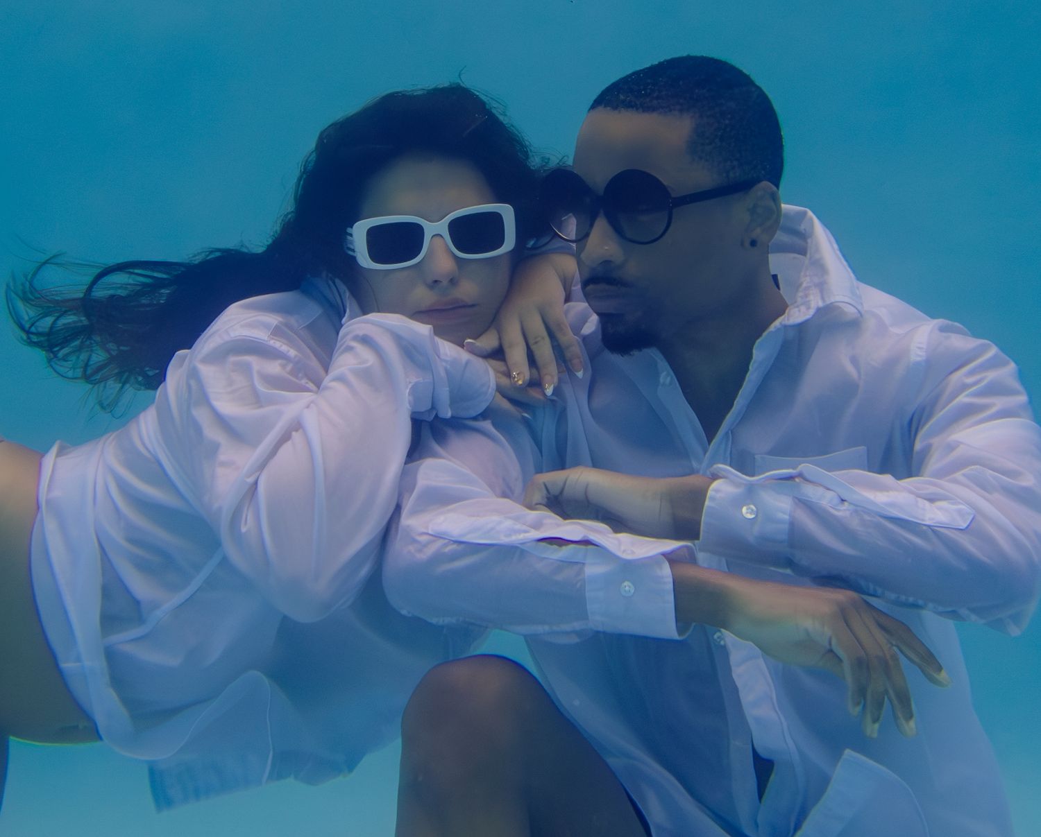 A sequence of underwater photos showing two people in white shirts swimming and embracing in a pool with blue water.