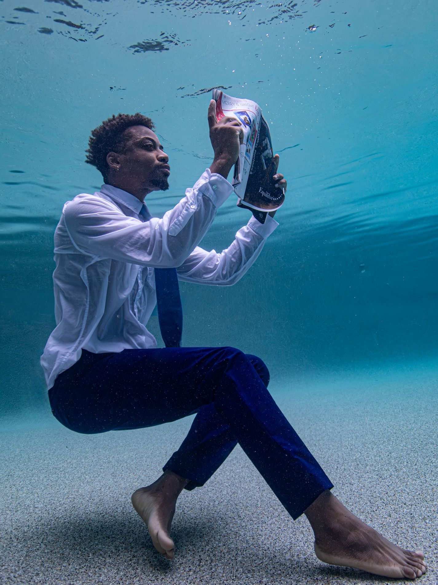 Figure in white shirt performing artistic movements underwater with vibrant blue background.