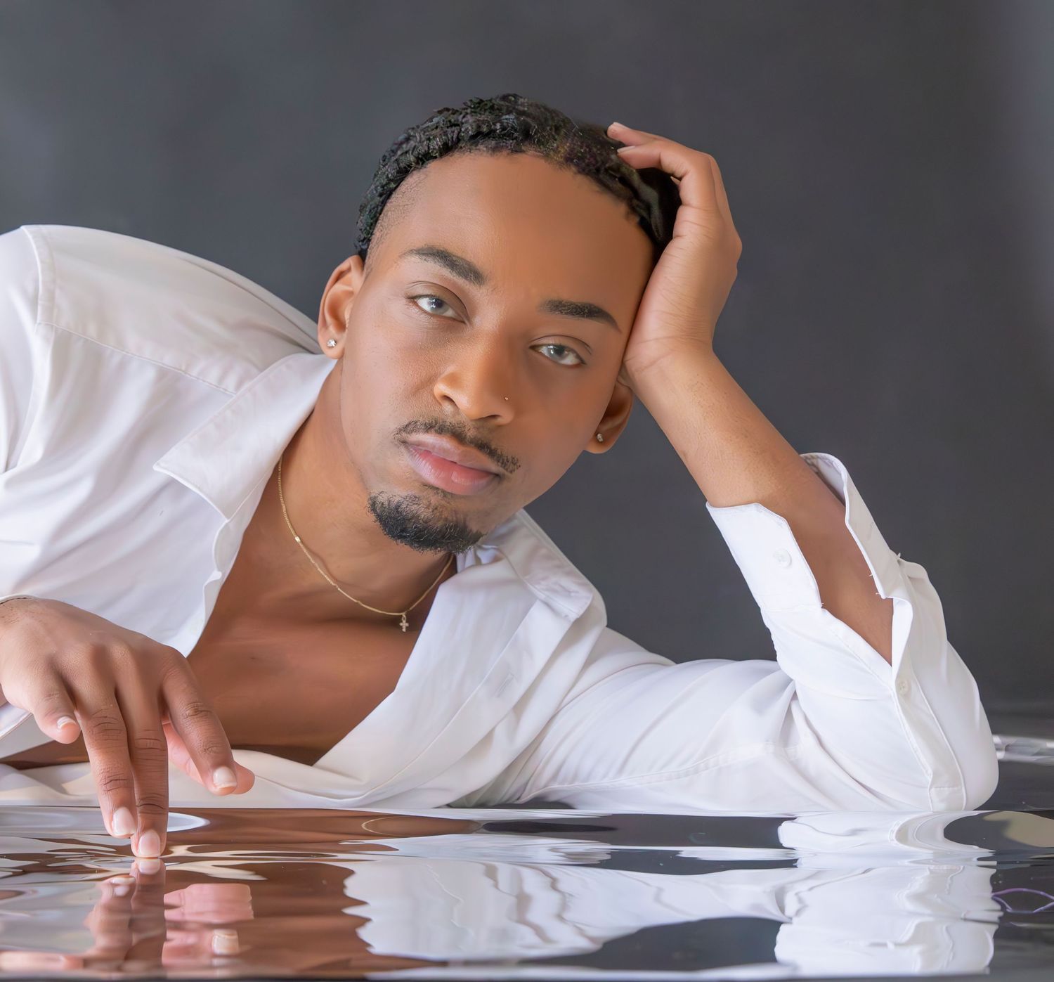Man person in a white button-down shirt poses while lying down against a reflective surface in a professional photoshoot.