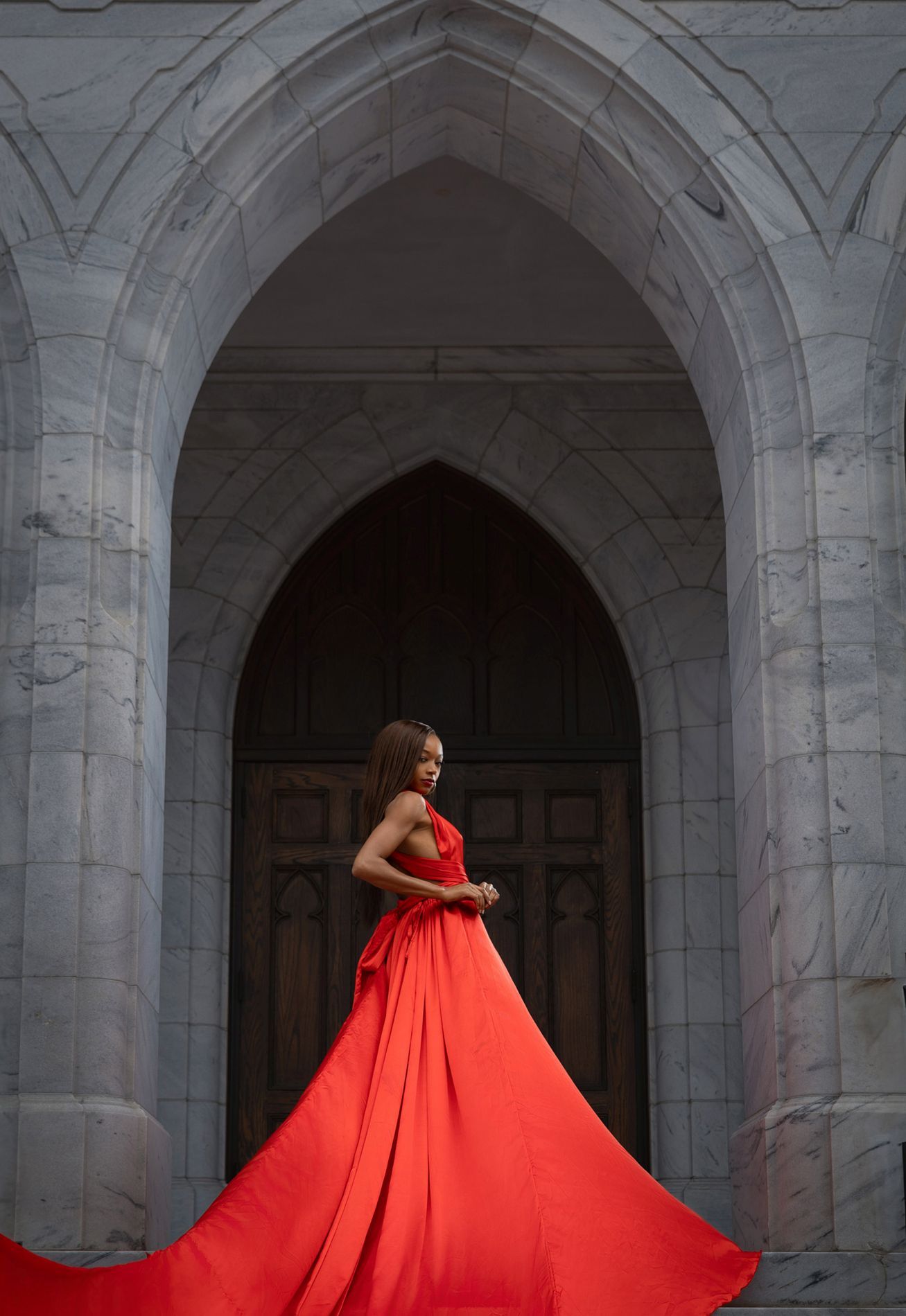 Flowing red gown creates dramatic movement in architectural stone archway setting.