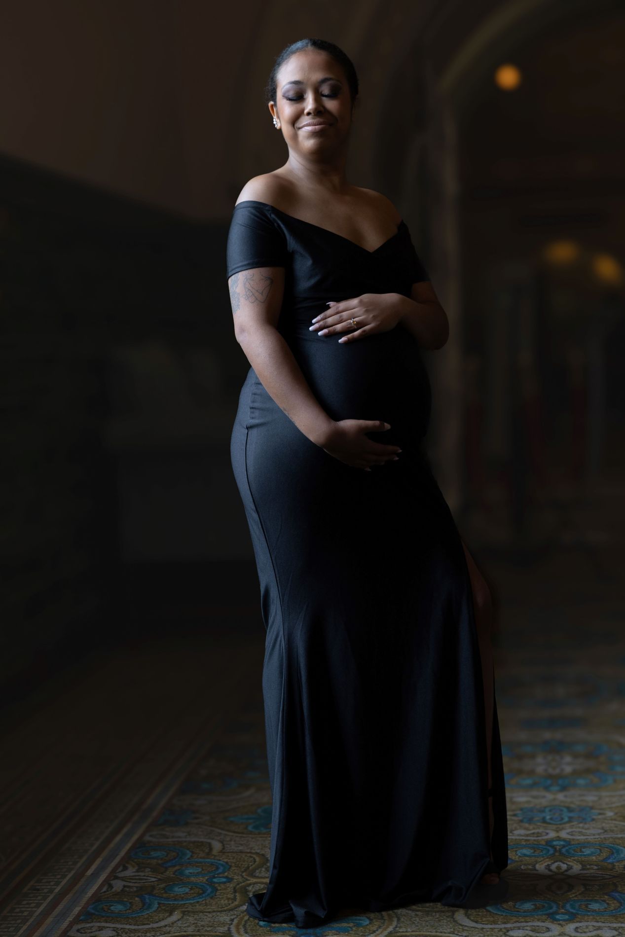 Elegant black dress portrait session on patterned carpet with dramatic low light atmosphere.