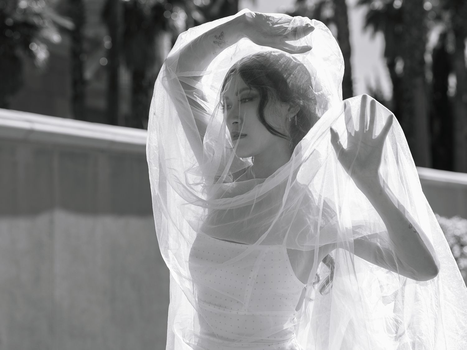 Black and white photo of a bride in a flowing white veil and gown, posing gracefully outdoors.