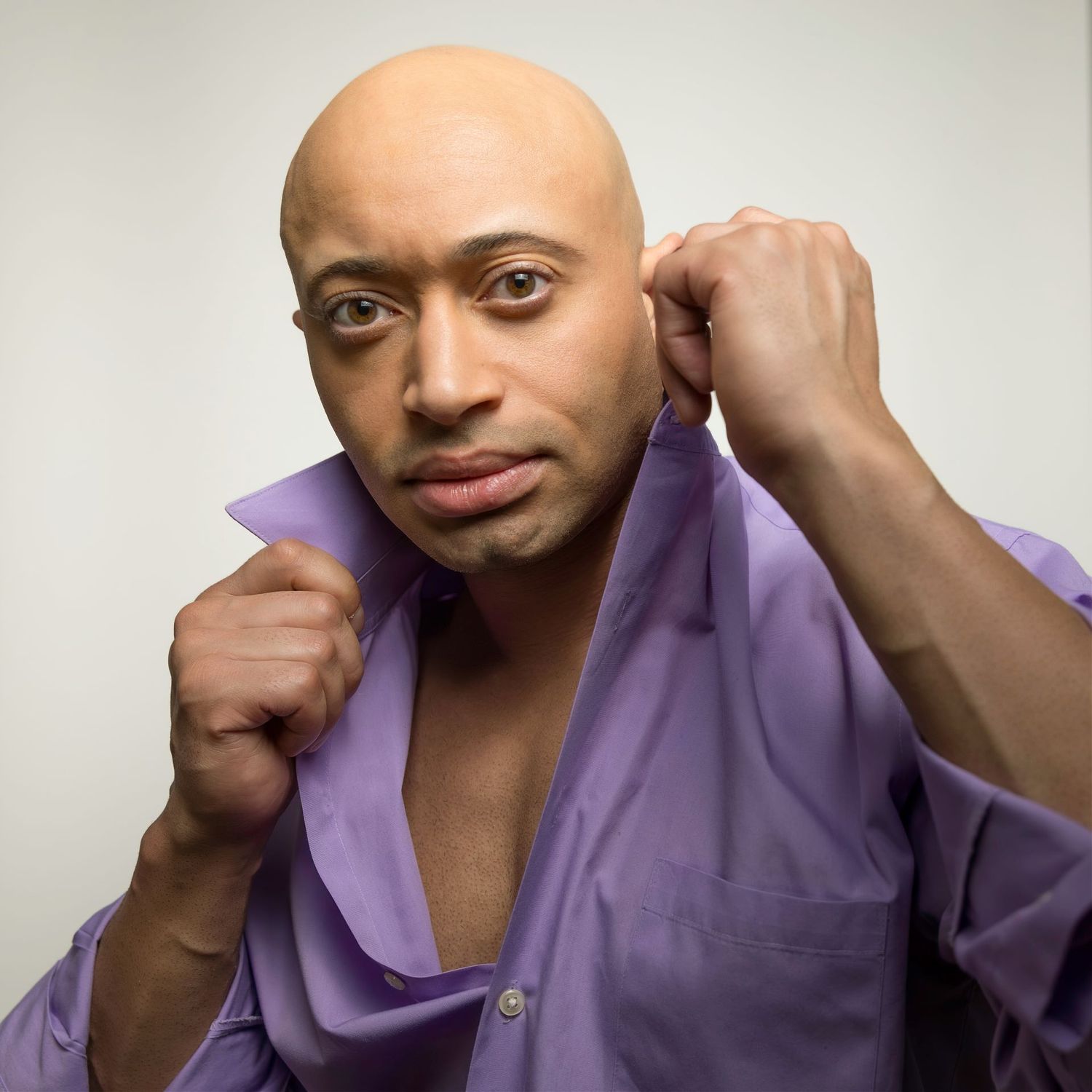 Portrait against gray background of person in purple button-down shirt with dramatic lighting.