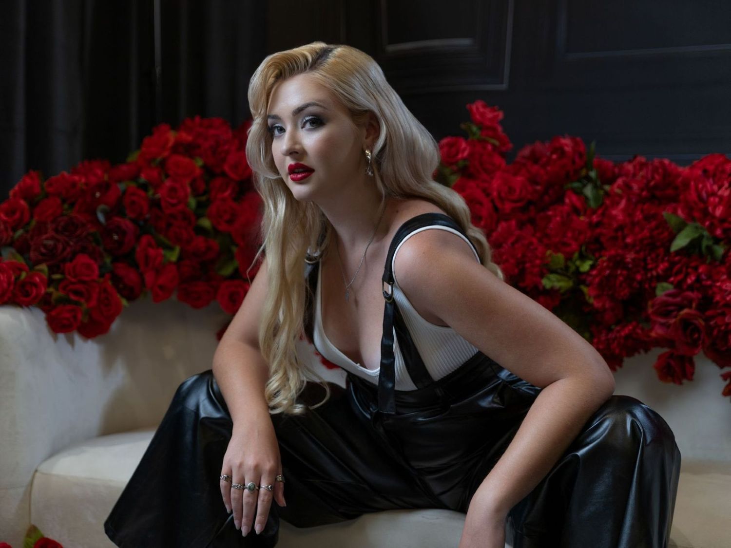 Woman in black dress poses next to vibrant red roses in elegant fashion photoshoot.