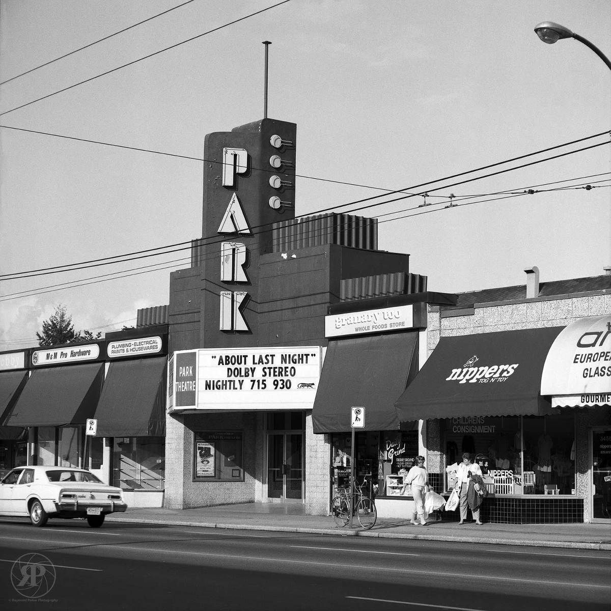 Vintage black and white photo of an art deco Park Theater with marquee and storefronts along a commercial street.