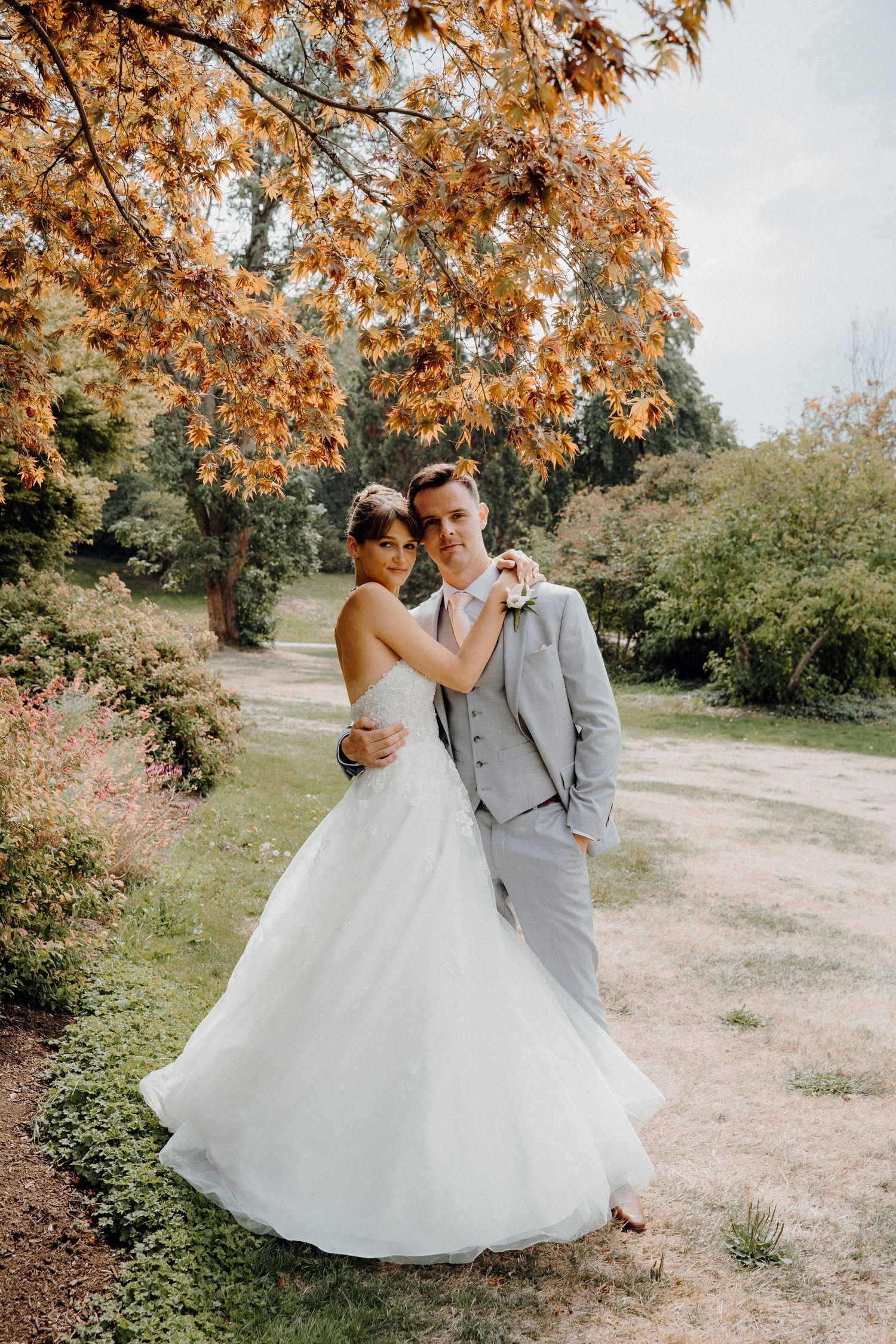 A romantic wedding couple dances beneath autumn trees with orange leaves in a dreamy outdoor setting.