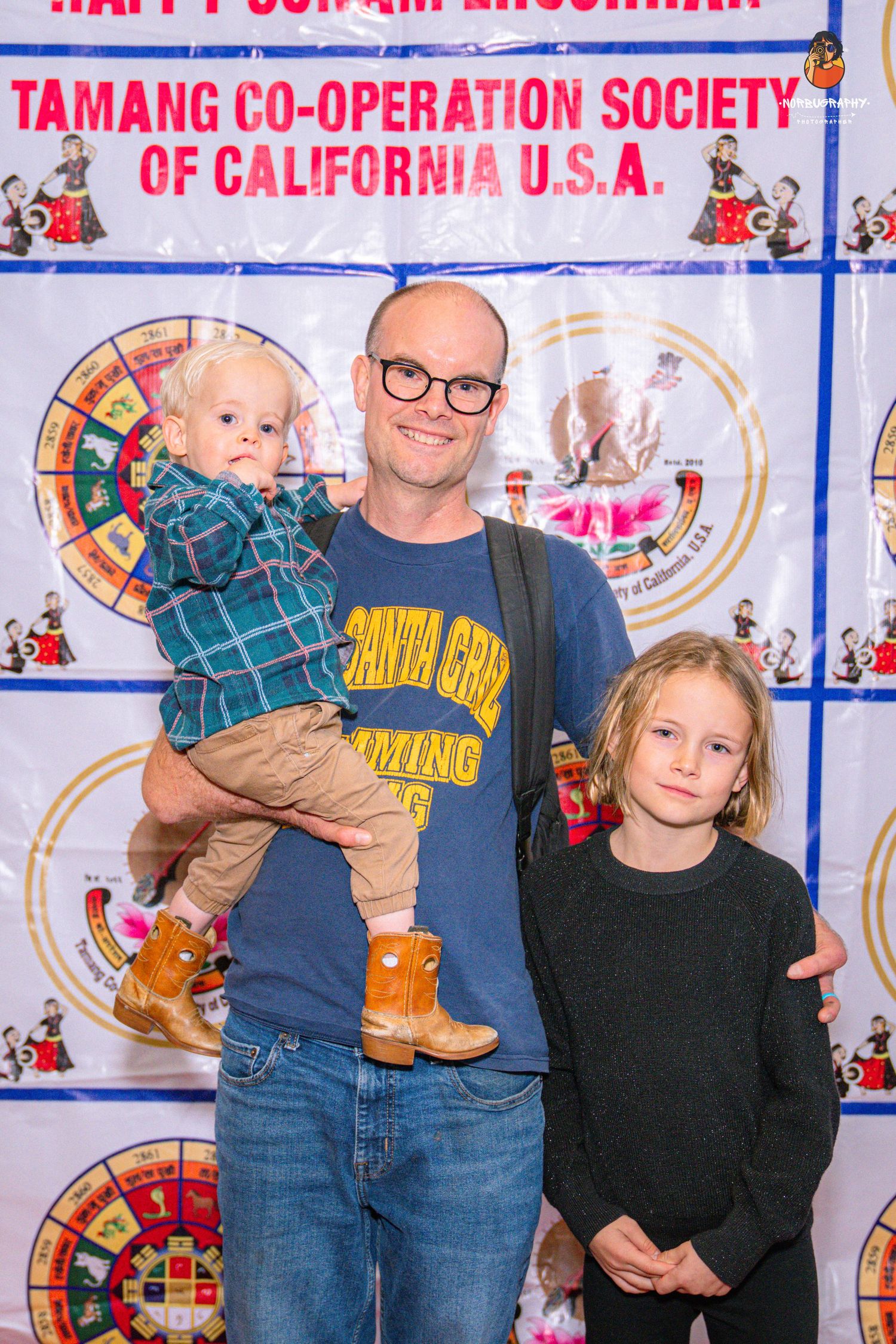 Family poses at Tamang Co-operation Society event backdrop with festive decorations.