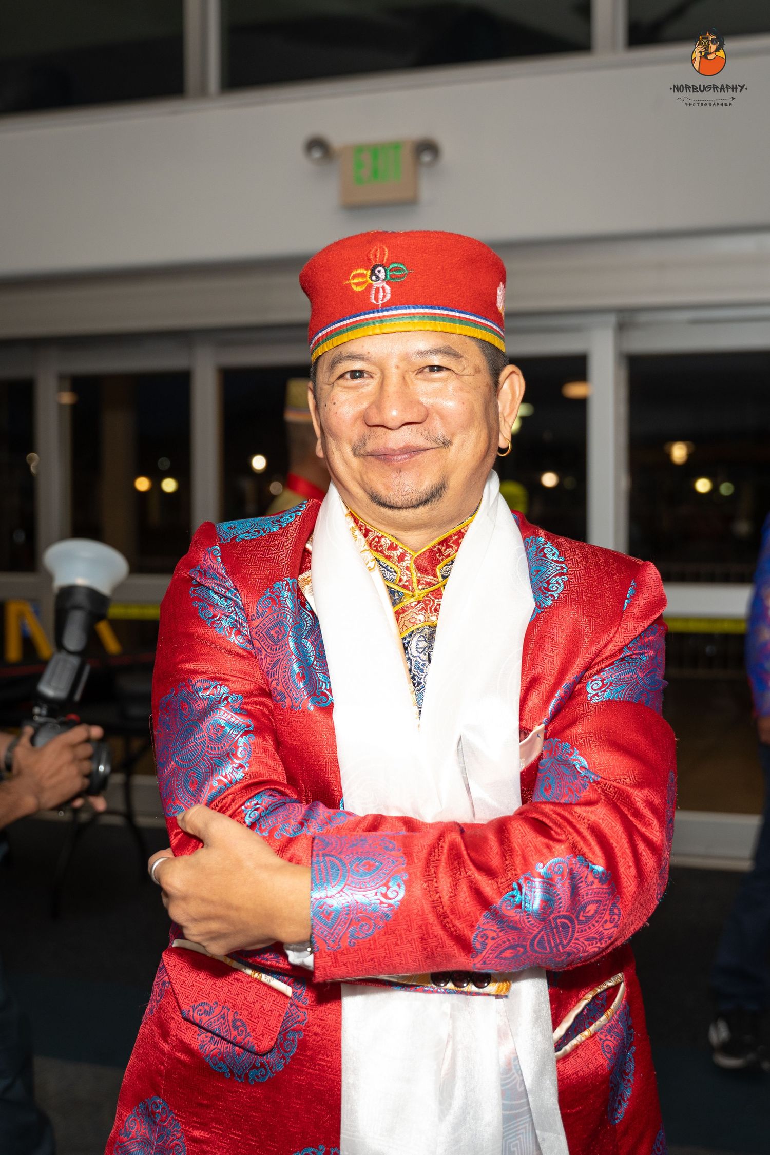 Person wearing red traditional jacket and ceremonial cap at cultural event.