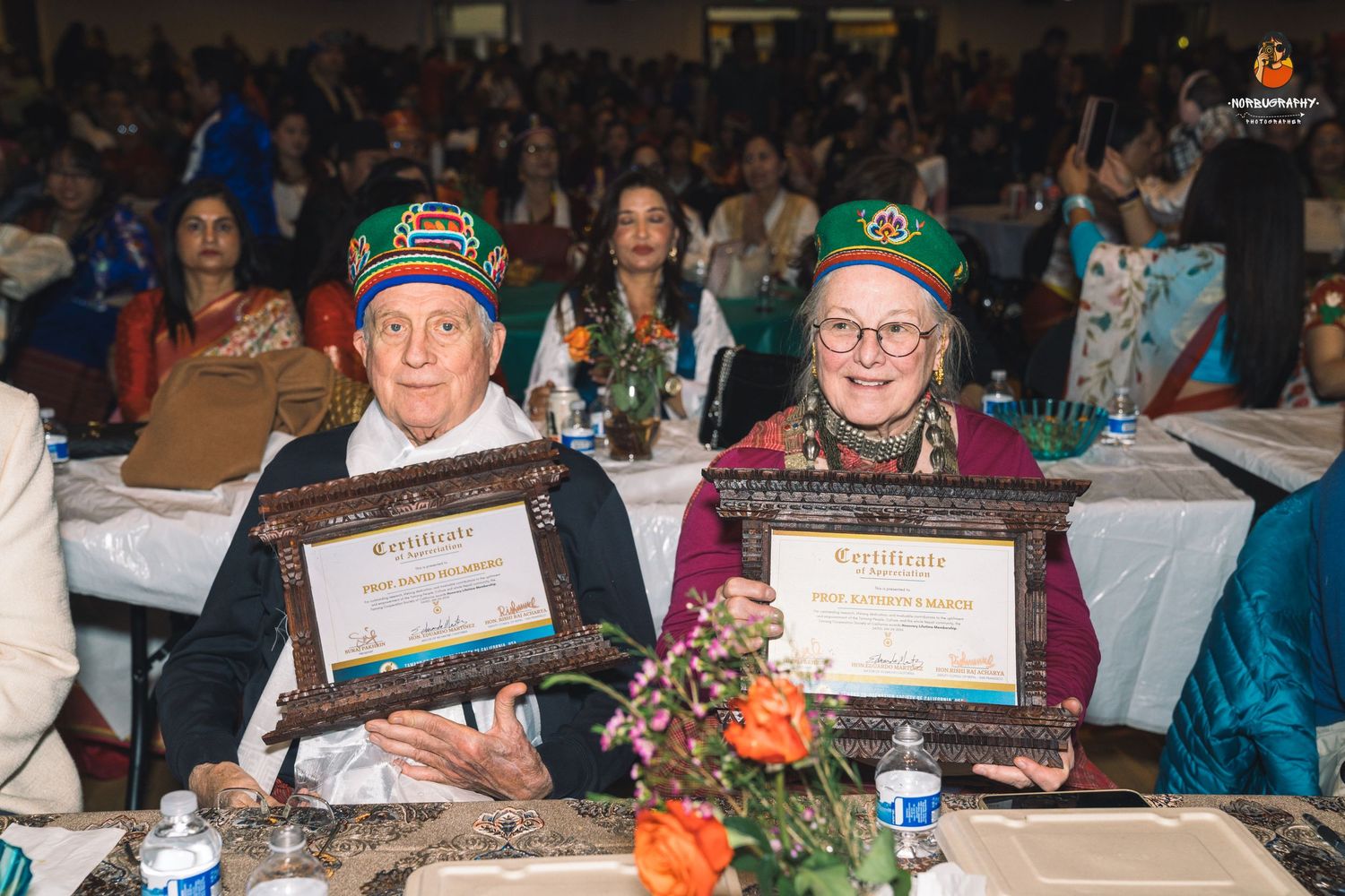 Award recipients display their certificates at a formal banquet with decorative table settings.