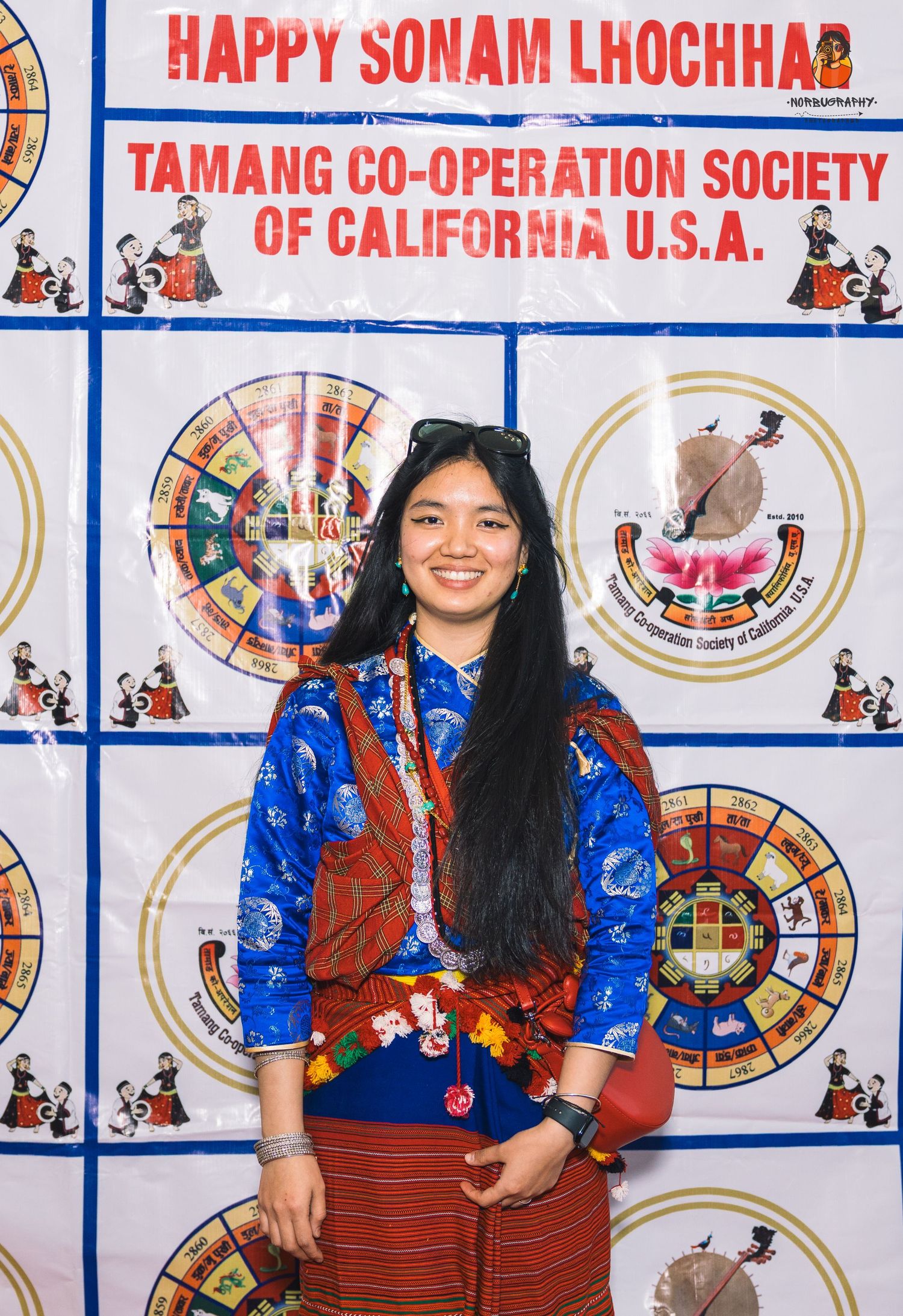Woman in traditional blue and red ethnic attire poses at Sonam Lhochhar celebration banner.