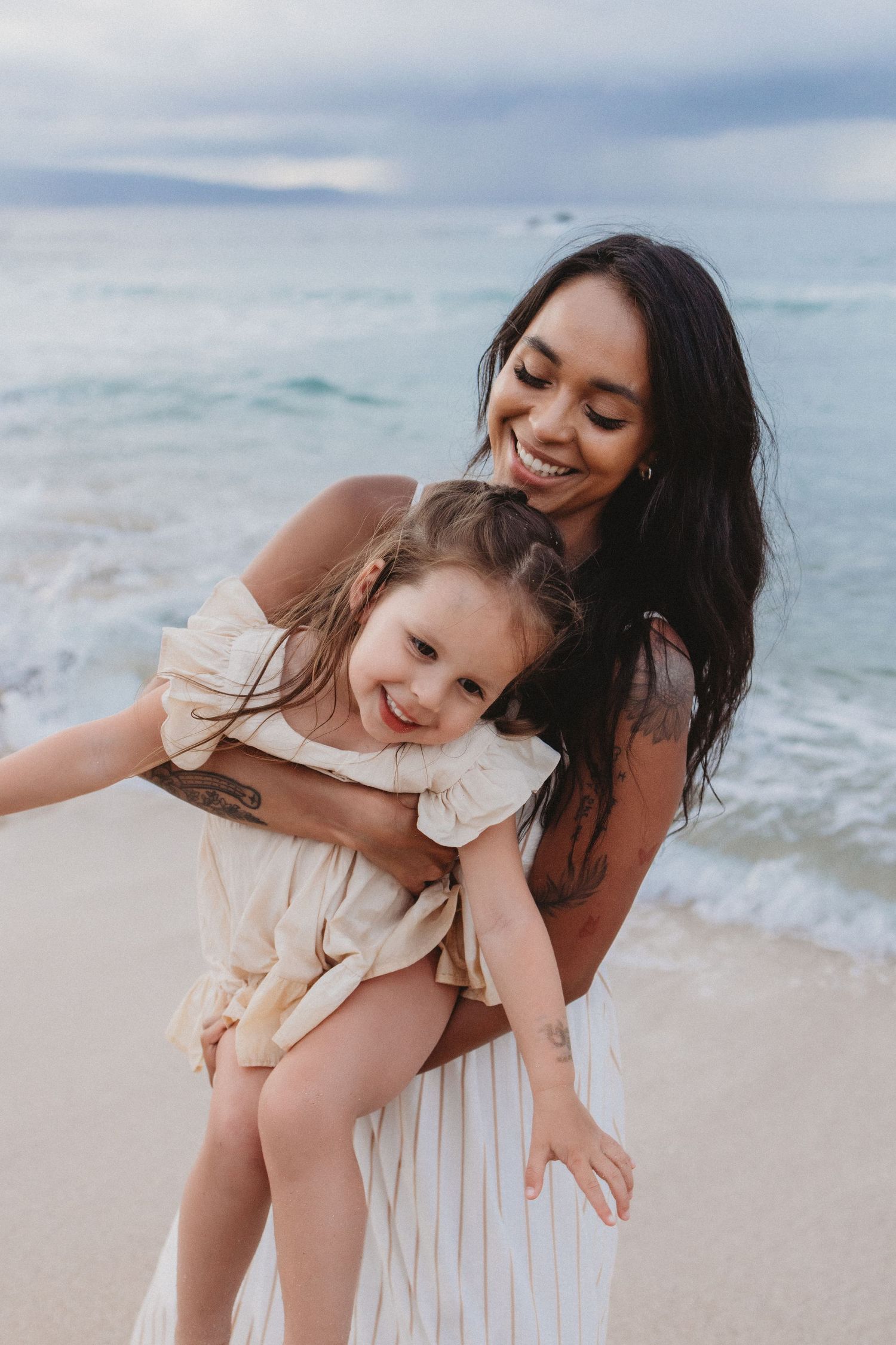 Maui family photography of mom swinging her daughter playfully by the ocean.