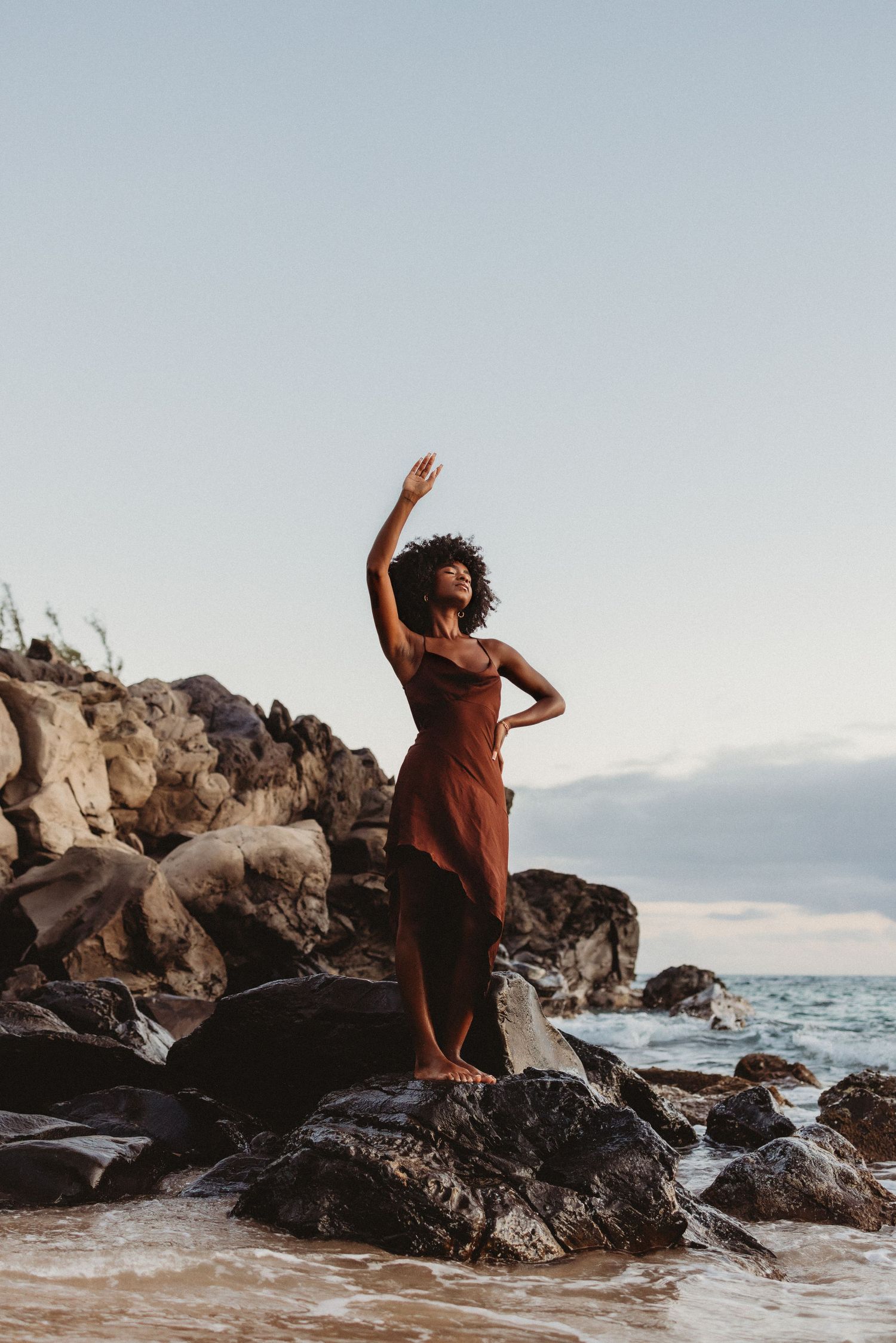 Lifestyle brand image featuring a woman posed on coastal rocks in the sea.