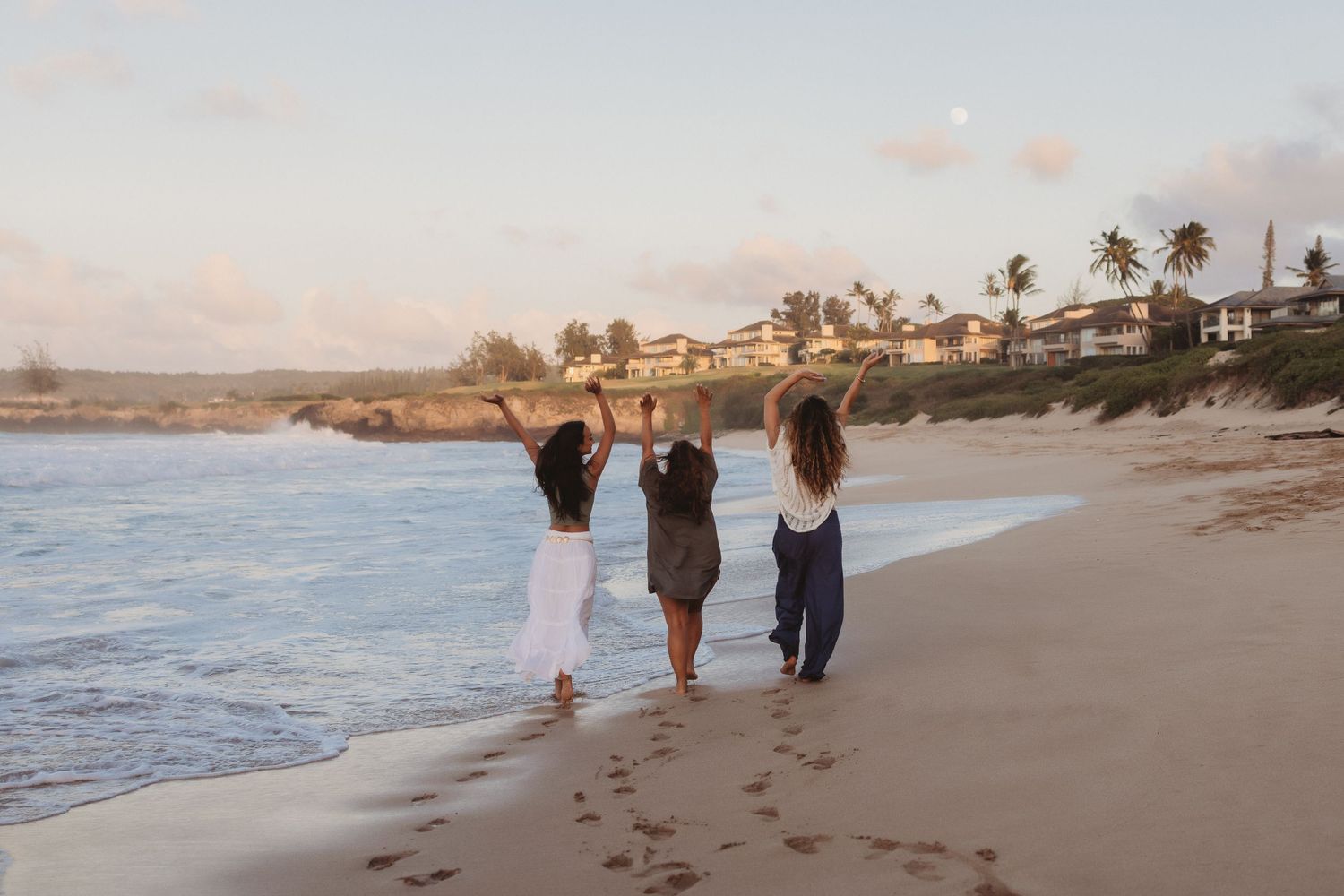Candid Maui portrait of sisters and mother joyfully lifting hands by the ocean.