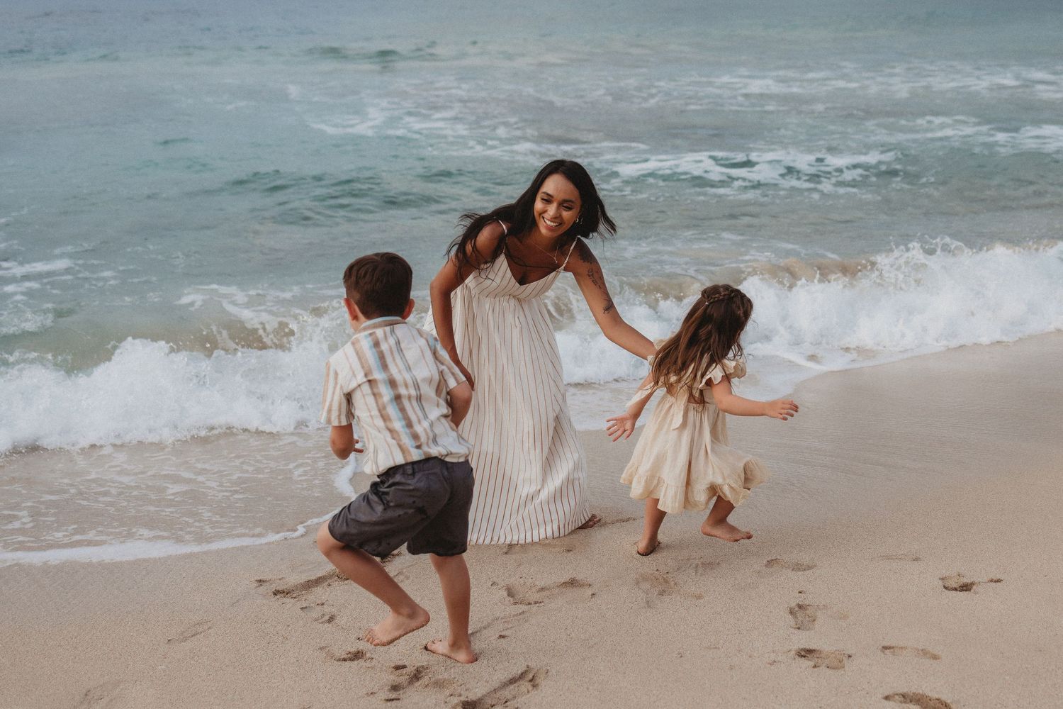 Family photo in Maui featuring mom and children running together on the beach.