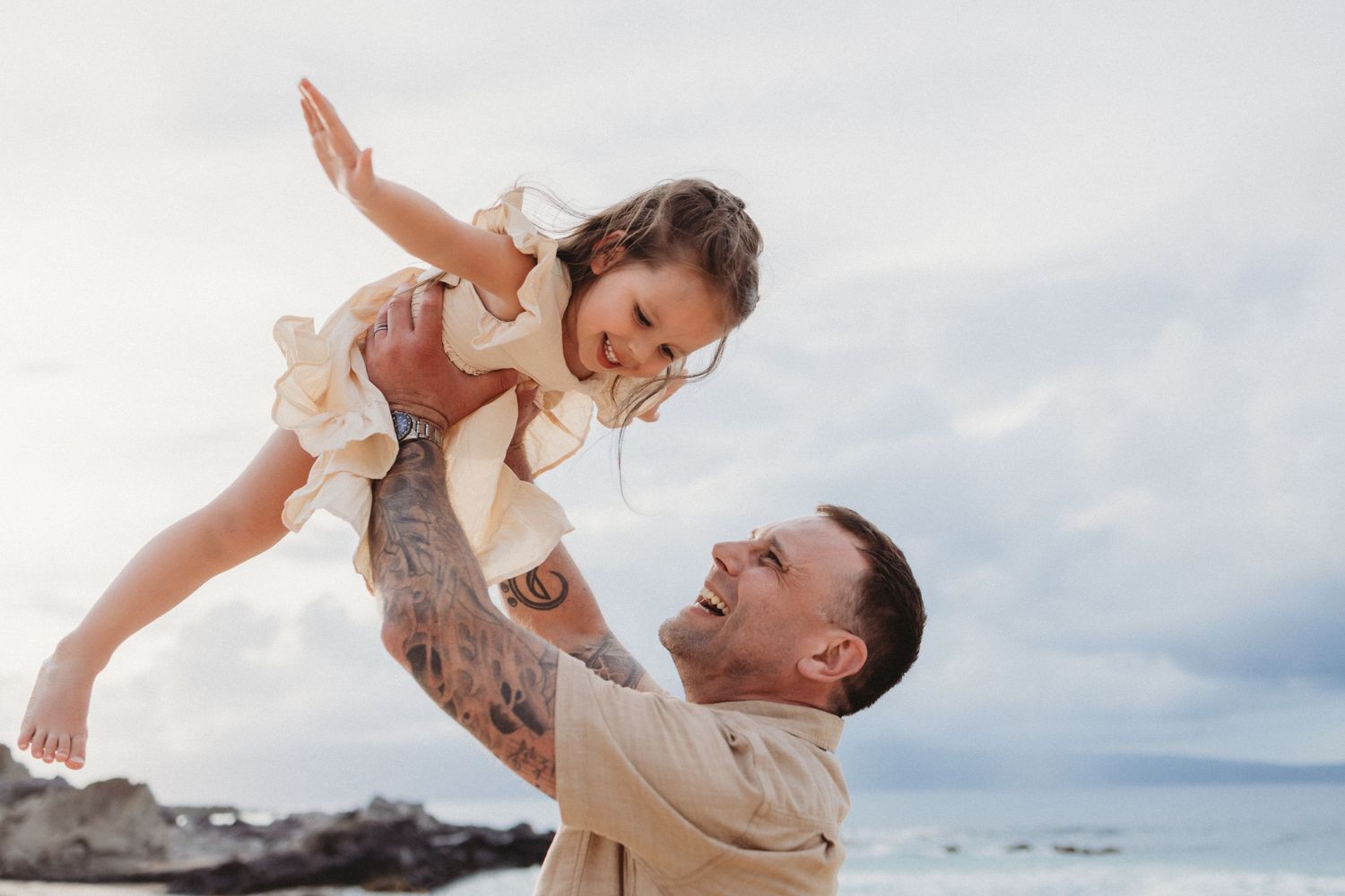 Maui family photography of dad lifting daughter in airplane pose by the beach.