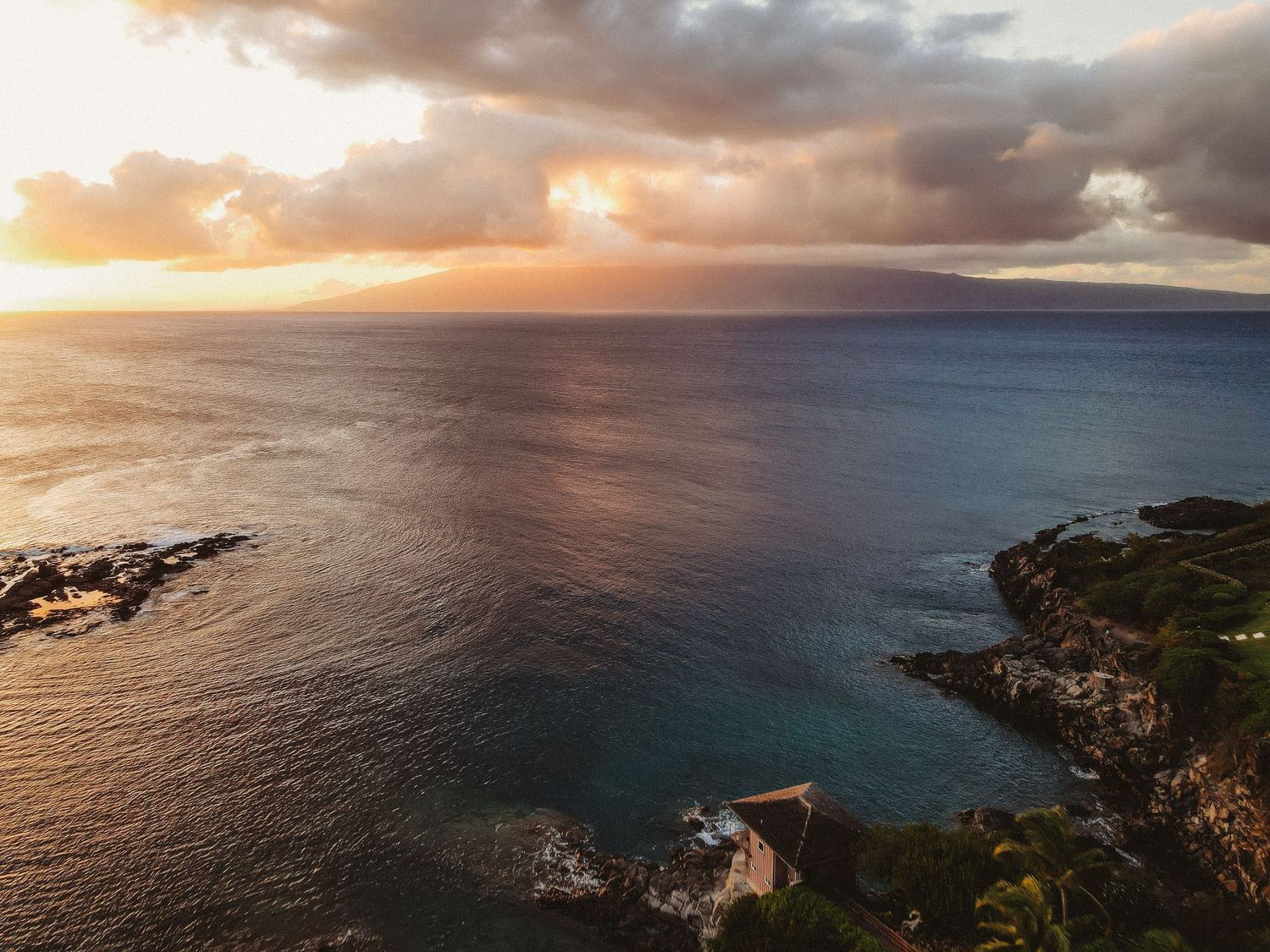 Aerial drone view of the ocean at sunset with golden light reflecting on the waves.