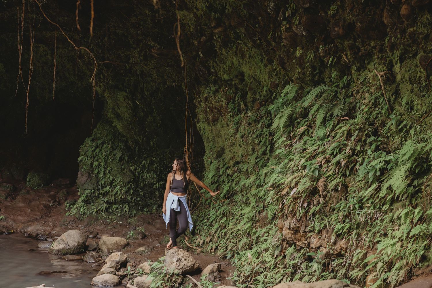 Lifestyle brand image featuring a woman framed by a cave and lush tropical background.